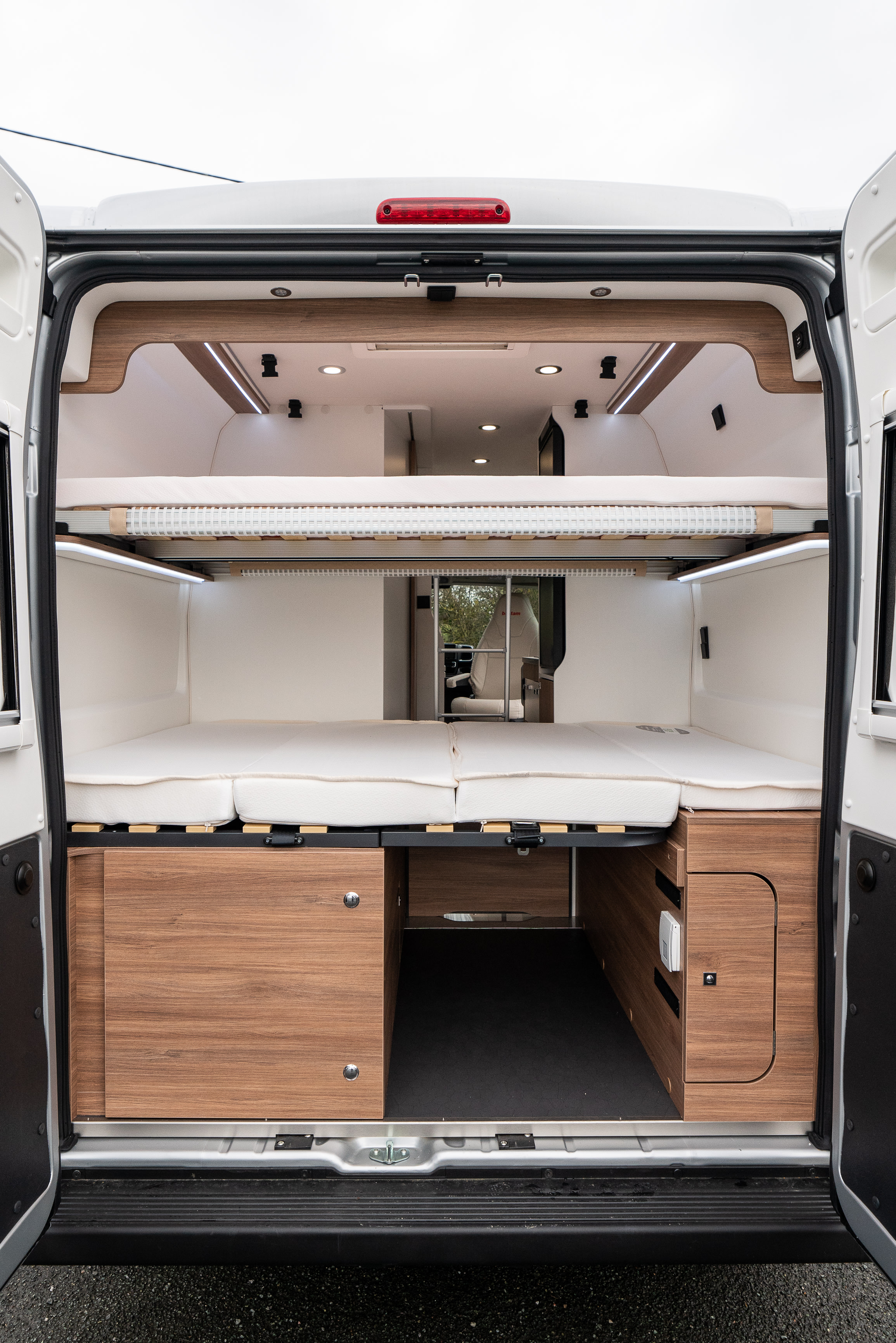 Rear view of RV rental interior: two levels of comfortable beds, integrated lighting, and wood storage cabinets.. Pilote V600 S ESSENTIEL 2024
