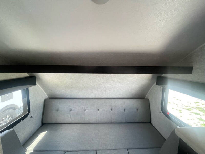 RV rental interior shows a cozy grey seating area, large windows, and an overhead bunk.. Braxton Creek Bushwhacker Plus 2024