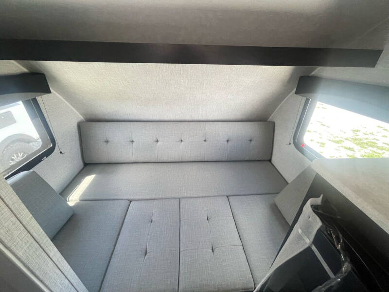 Spacious grey interior of an **rv rental**, featuring a convertible seating/bed, large windows, and overhead storage.. Braxton Creek Bushwhacker Plus 2024