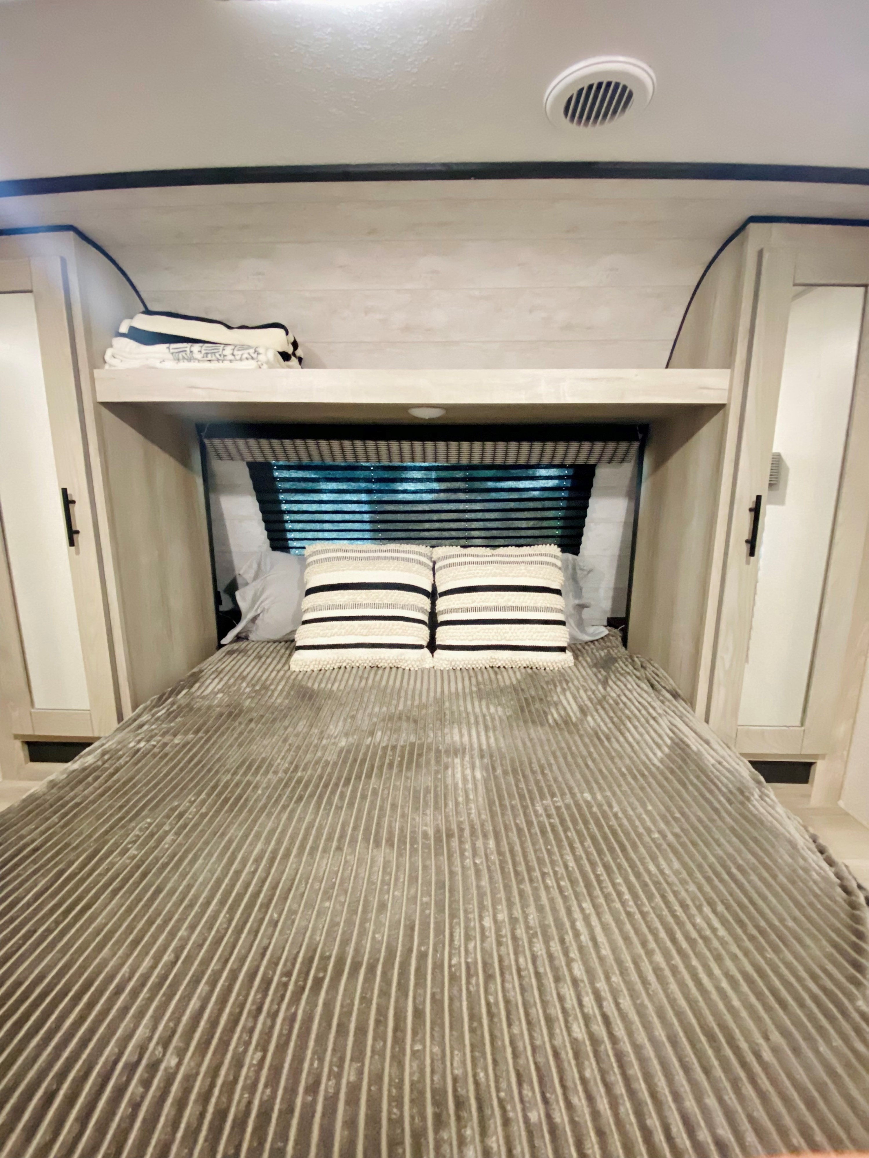 Inside a comfortable RV rental bedroom, featuring a striped bed, overhead shelf, and side cabinets.. Connect SE 2022
