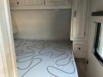 Compact RV rental bedroom with patterned mattress, overhead cabinets, and side window for a comfortable stay.. East to West Della Terra 250BH 2023