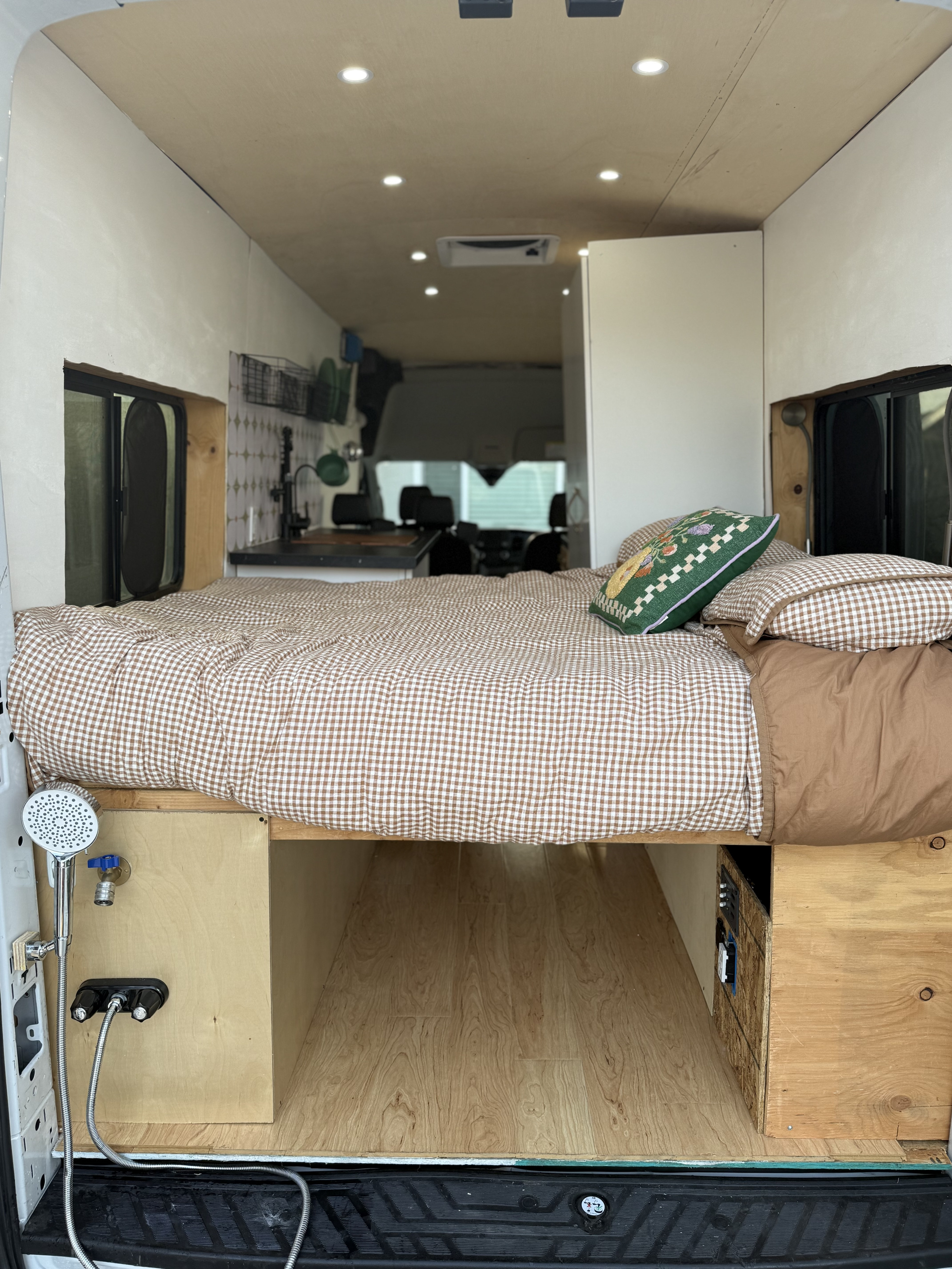 Inside a modern rv rental camper van: comfortable bed with gingham bedding, kitchen, and outdoor shower setup.. Ford Transit 2021