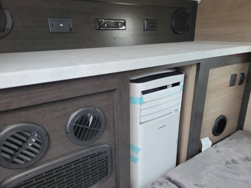 This RV rental interior features a white portable AC unit, multiple power outlets, a stereo, and vents, ensuring a comfortable journey.. Braxton Creek Bushwhacker 2024