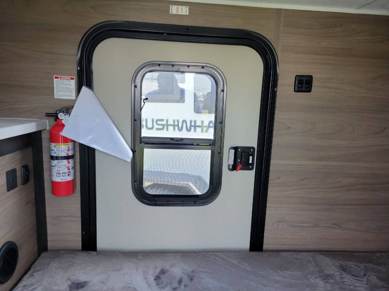 RV rental interior: exit door with fire extinguisher, bunk, wood paneling, and "BUSHWHACKER" text visible.. Braxton Creek Bushwhacker 2024