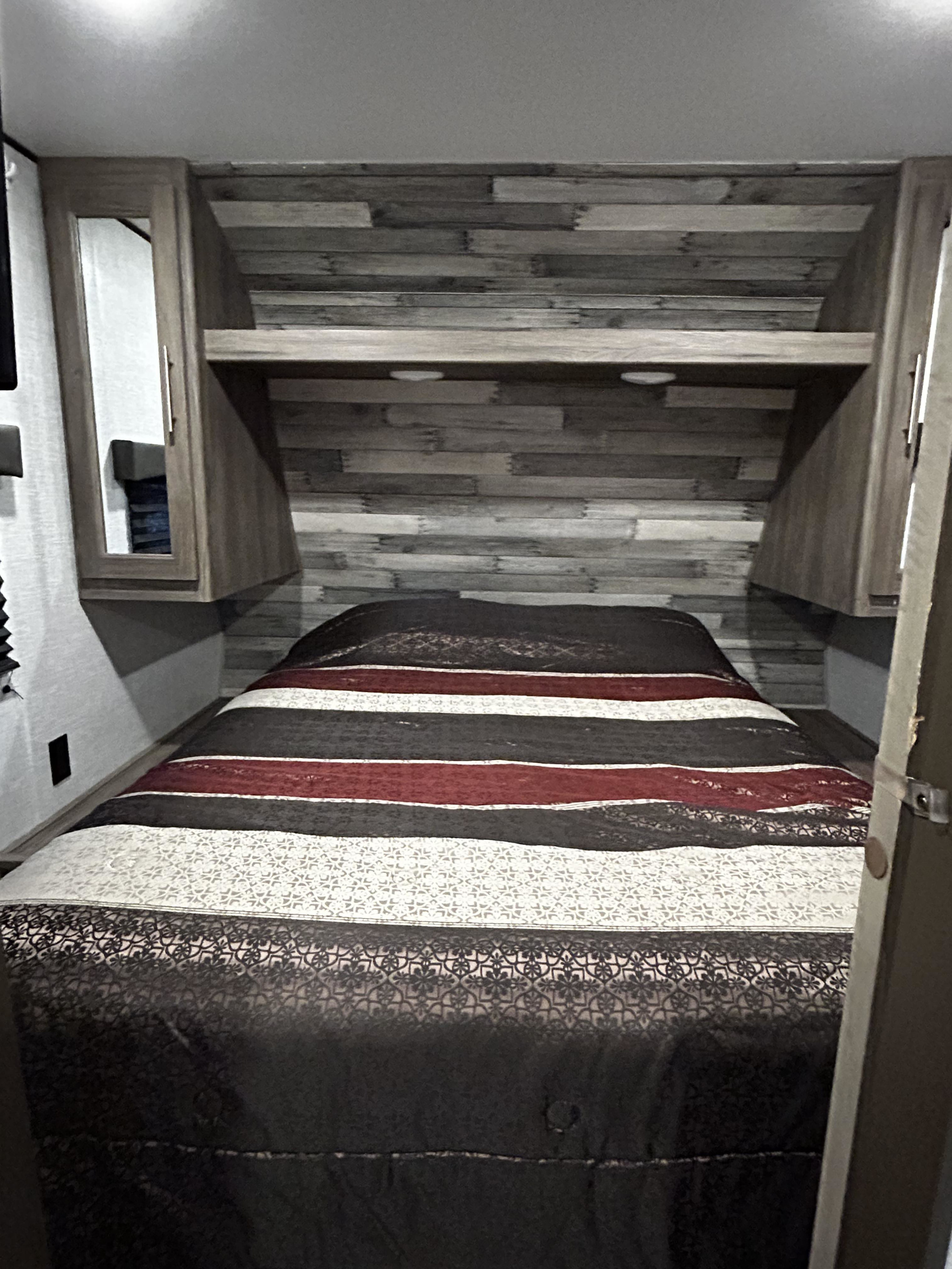 Cozy RV rental bedroom: Striped comforter on bed, compact wooden headboard & storage. Ideal for travel.. Crossroads RV Zinger 2021