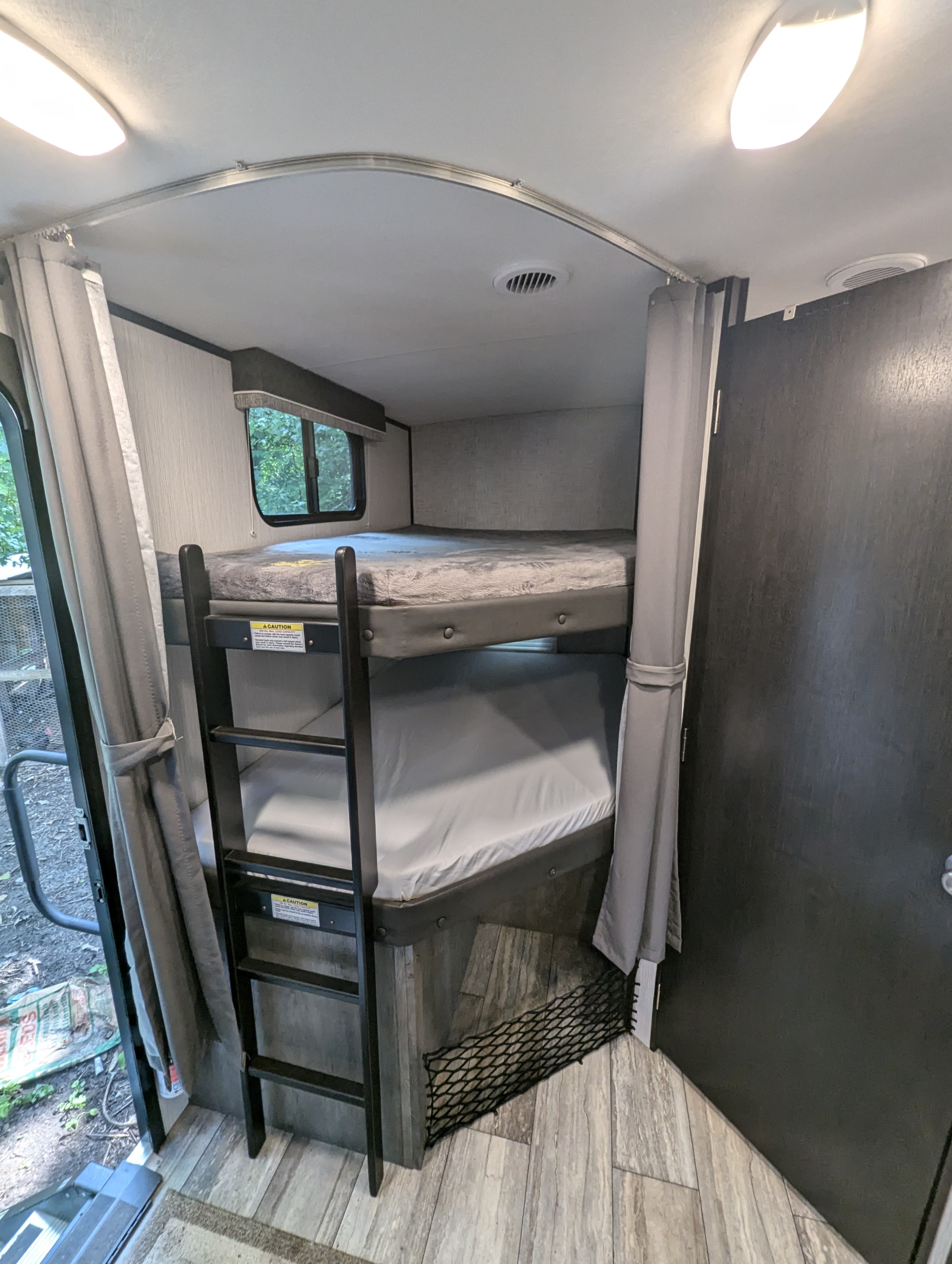 RV rental bunk beds with a ladder, window, and privacy curtains. Inside a modern RV.. Heartland RVs North Trail 2021