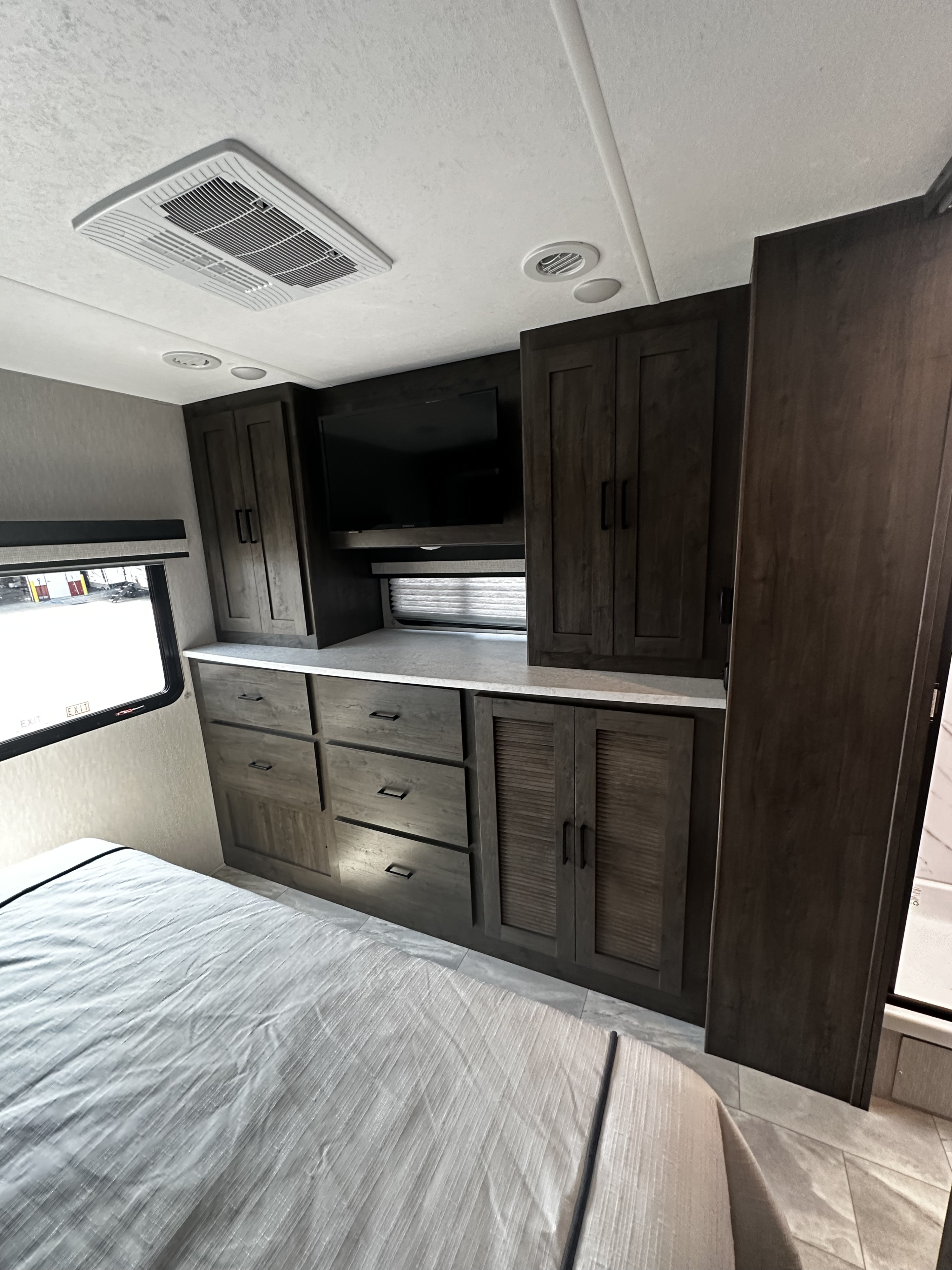 Step into this rv rental's cozy bedroom featuring ample built-in storage, a wall-mounted TV, and an overhead AC unit.. Coachmen 31TS 2023