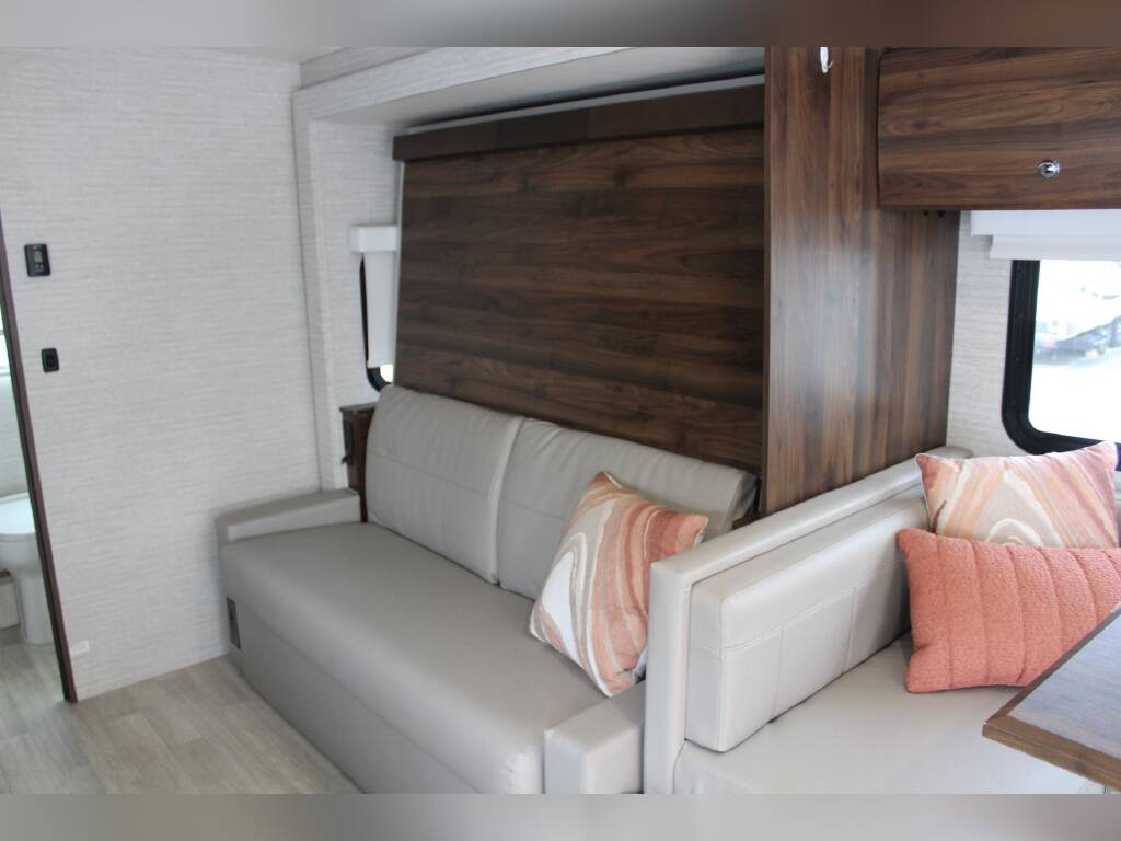 RV rental's inviting interior: light sofas, accent pillows, rich wood paneling, and a discreet murphy bed. Perfect for living/sleeping.. Winnebago Navion 2022