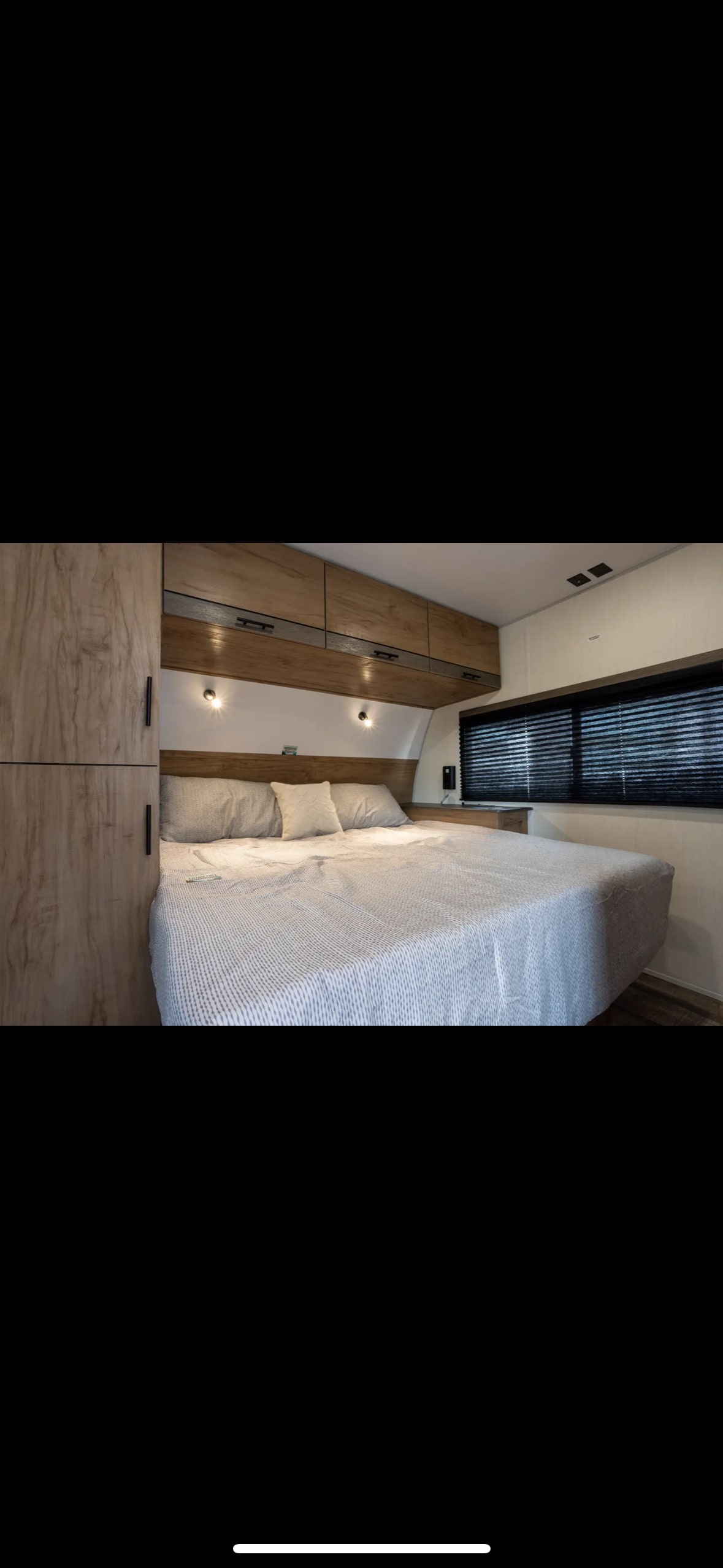 Comfortable RV bedroom featuring a cozy bed, overhead cabinets, and window blinds. Ideal for your next RV rental adventure.. Forest River Campsite Reserve 2025