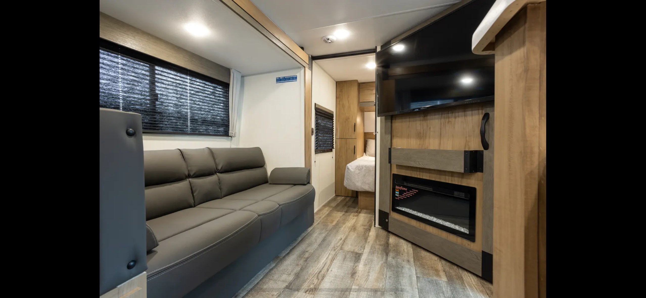 Modern RV rental living area with comfy sofa, TV, fireplace, and adjoining bedroom.. Forest River Campsite Reserve 2025
