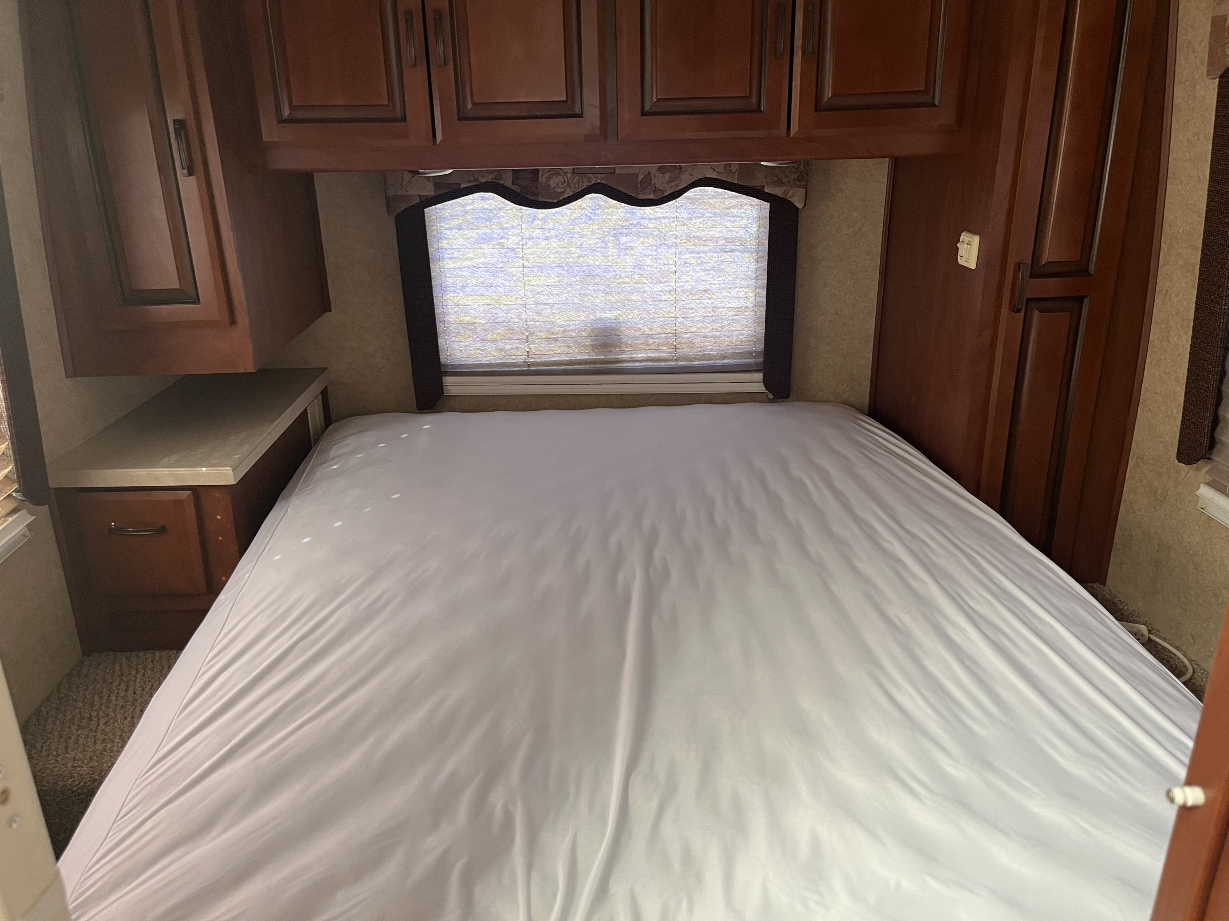 Step inside this cozy RV rental bedroom, featuring a comfortable bed, ample storage cabinets, and a window with blinds.. Lexington Grand Touring 2010
