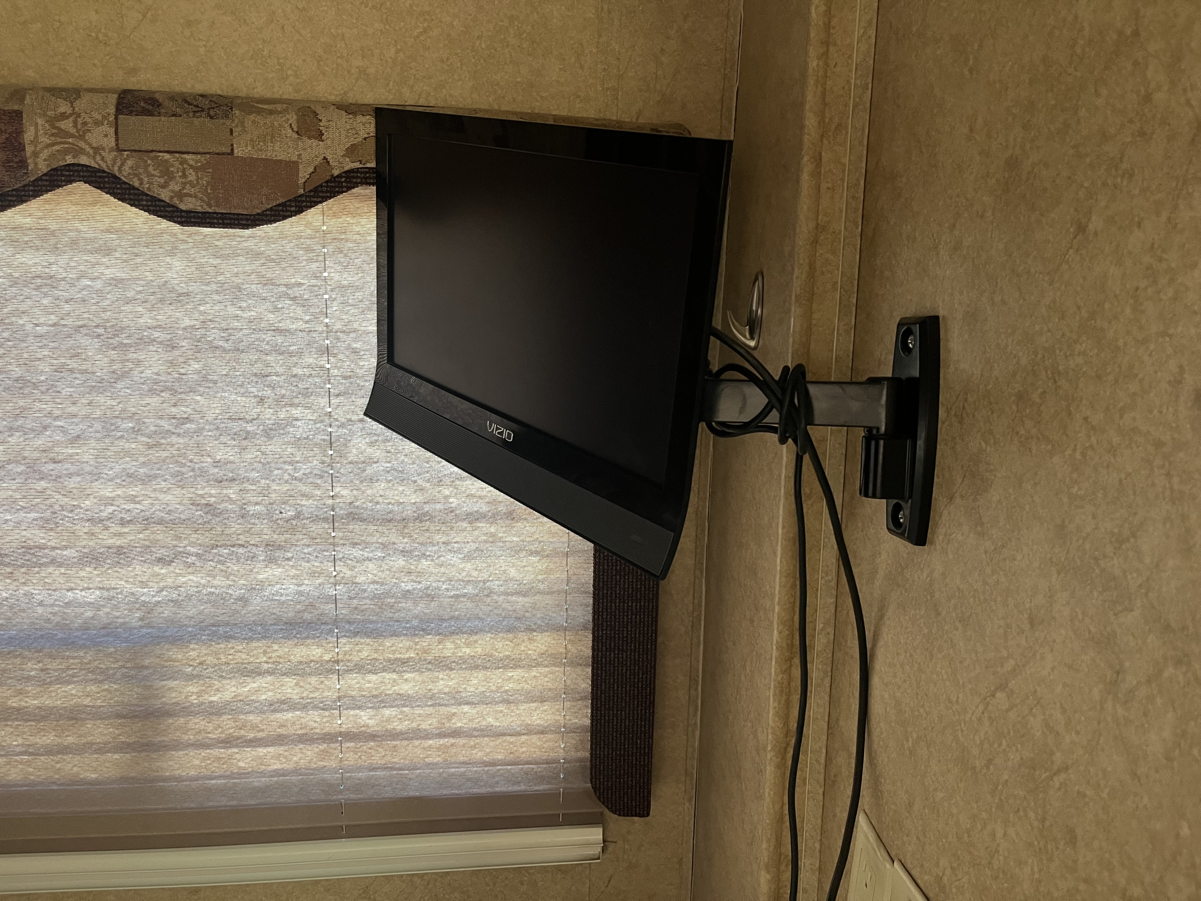 Small VIZIO TV on an articulating mount in an rv rental, with black cables, next to a window with pleated blinds.. Lexington Grand Touring 2010