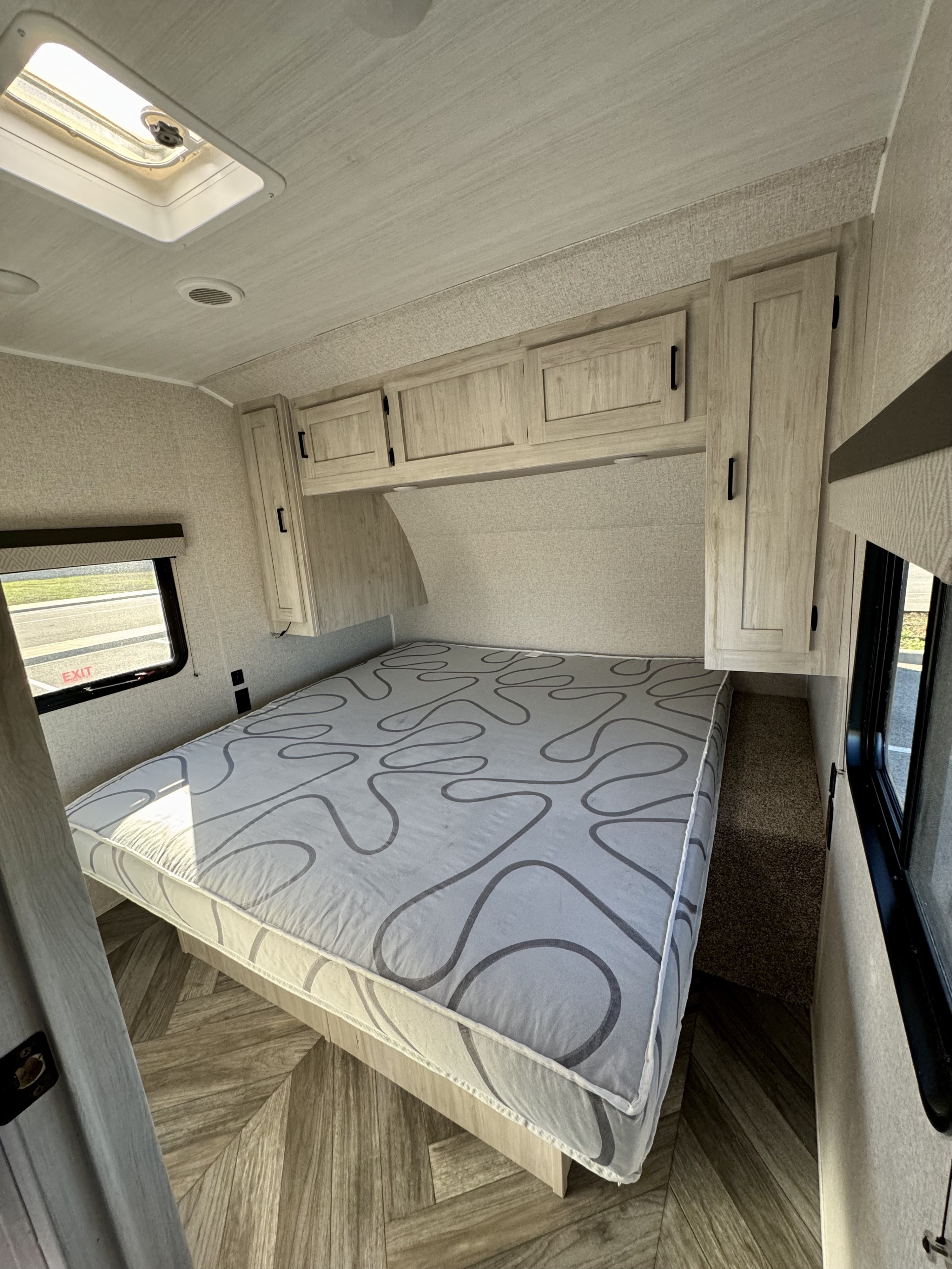 Bright RV rental bedroom with a patterned mattress, light wood cabinets, a skylight, and large windows. Ideal for travel.. East to West Della Terra LE 2024