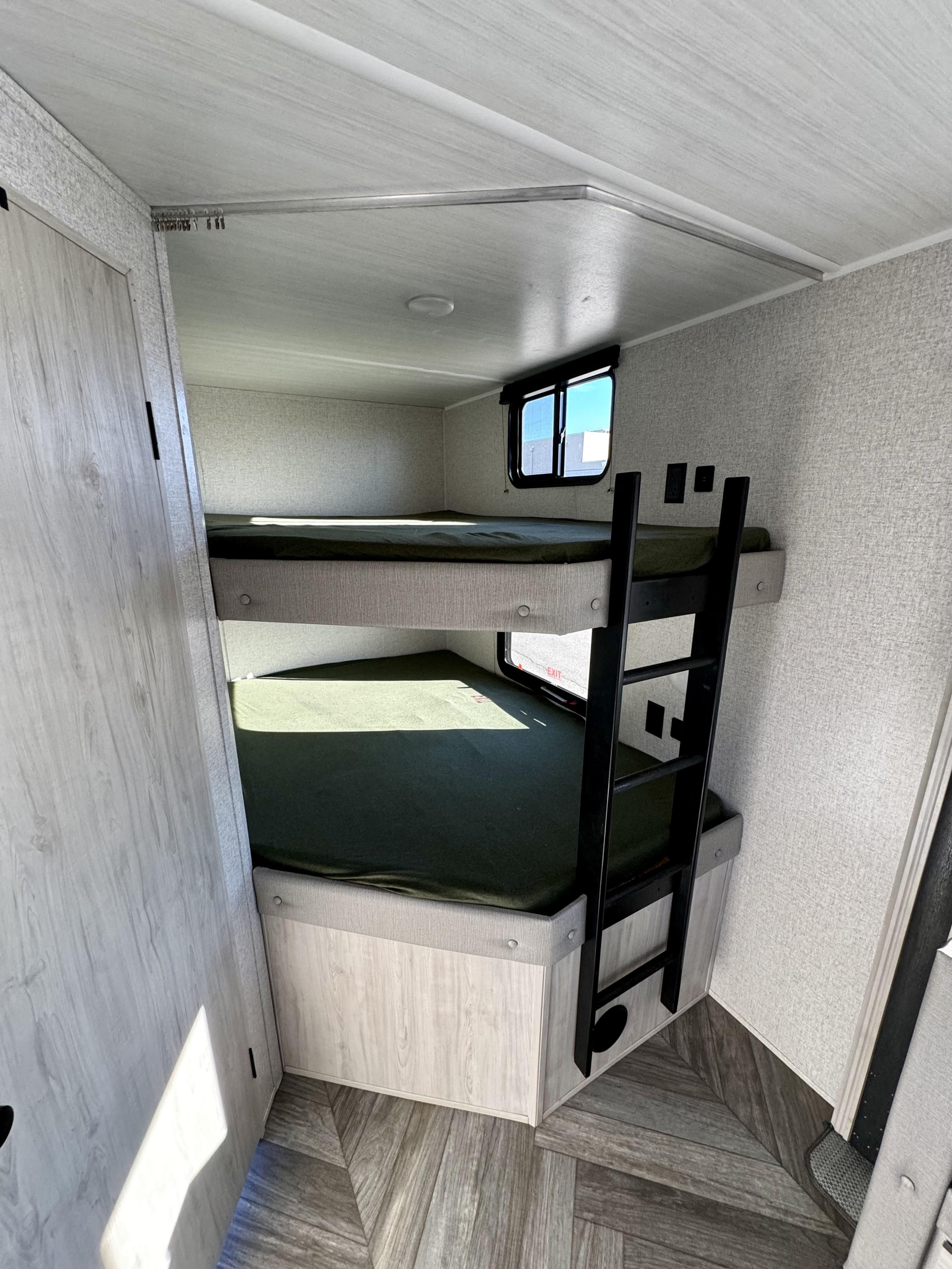 Cozy RV rental interior featuring two bunk beds with green sheets, a ladder, and a window for compact sleeping.. East to West Della Terra LE 2024