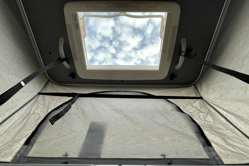 RV rental interior with an open pop-top skylight, revealing cloudy skies above the fabric walls.. Thor Scope 2023