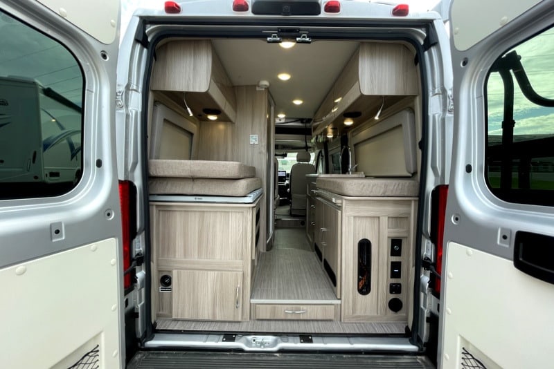 Open rear view of a modern RV rental camper van's interior, featuring light wood cabinets, bed, and kitchen area.. Thor Scope 2023