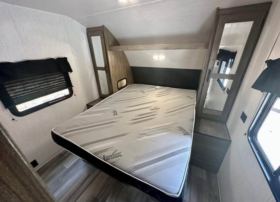 RV rental bedroom with a comfortable mattress, mirrored wardrobes, and side windows with blinds for your travels.. Heartland RVs Pioneer 2023