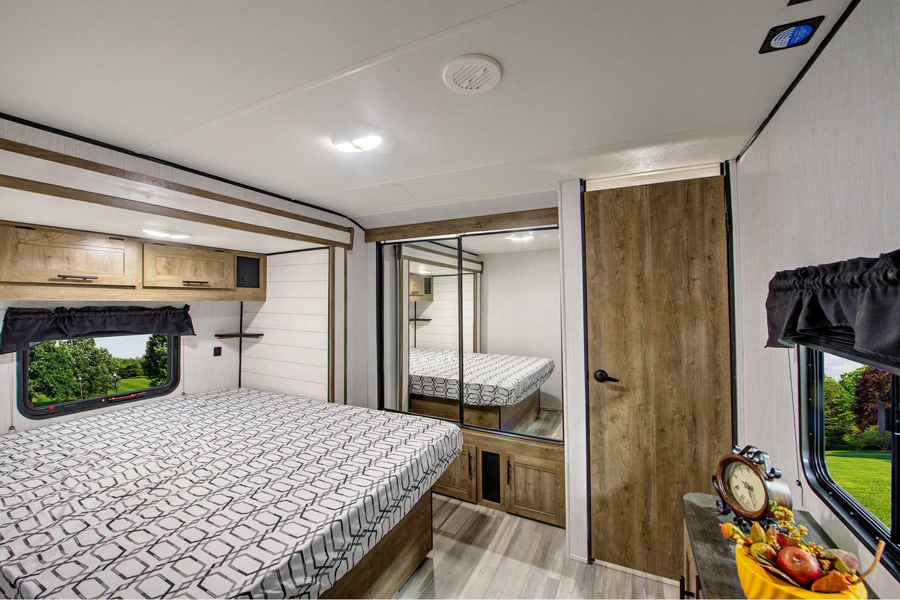 Spacious RV rental bedroom with a comfortable bed, overhead cabinets, mirrored closet, and scenic window view.. Heartland RVs Pioneer 2022