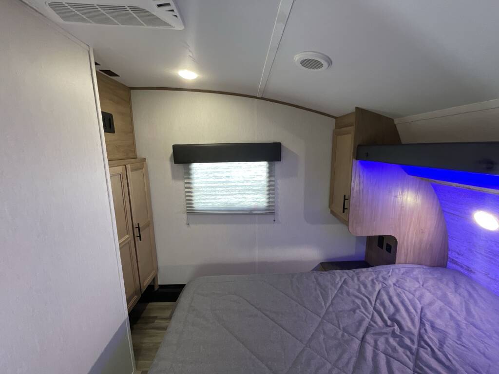 RV rental bedroom interior with a comfy bed, window, overhead cabinets, and cool blue accent lighting.. Forest River Cherokee 2023