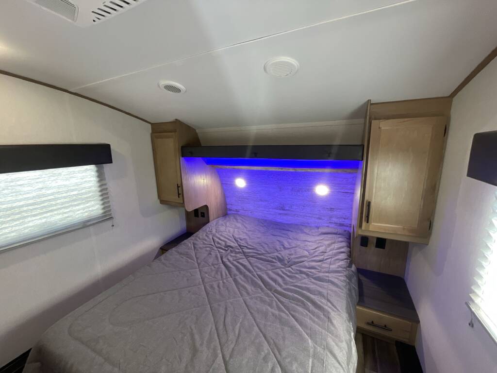 RV rental bedroom: a comfortable bed with grey comforter, wooden cabinets, and blue LED lighting creates a cozy sleeping space.. Forest River Cherokee 2023