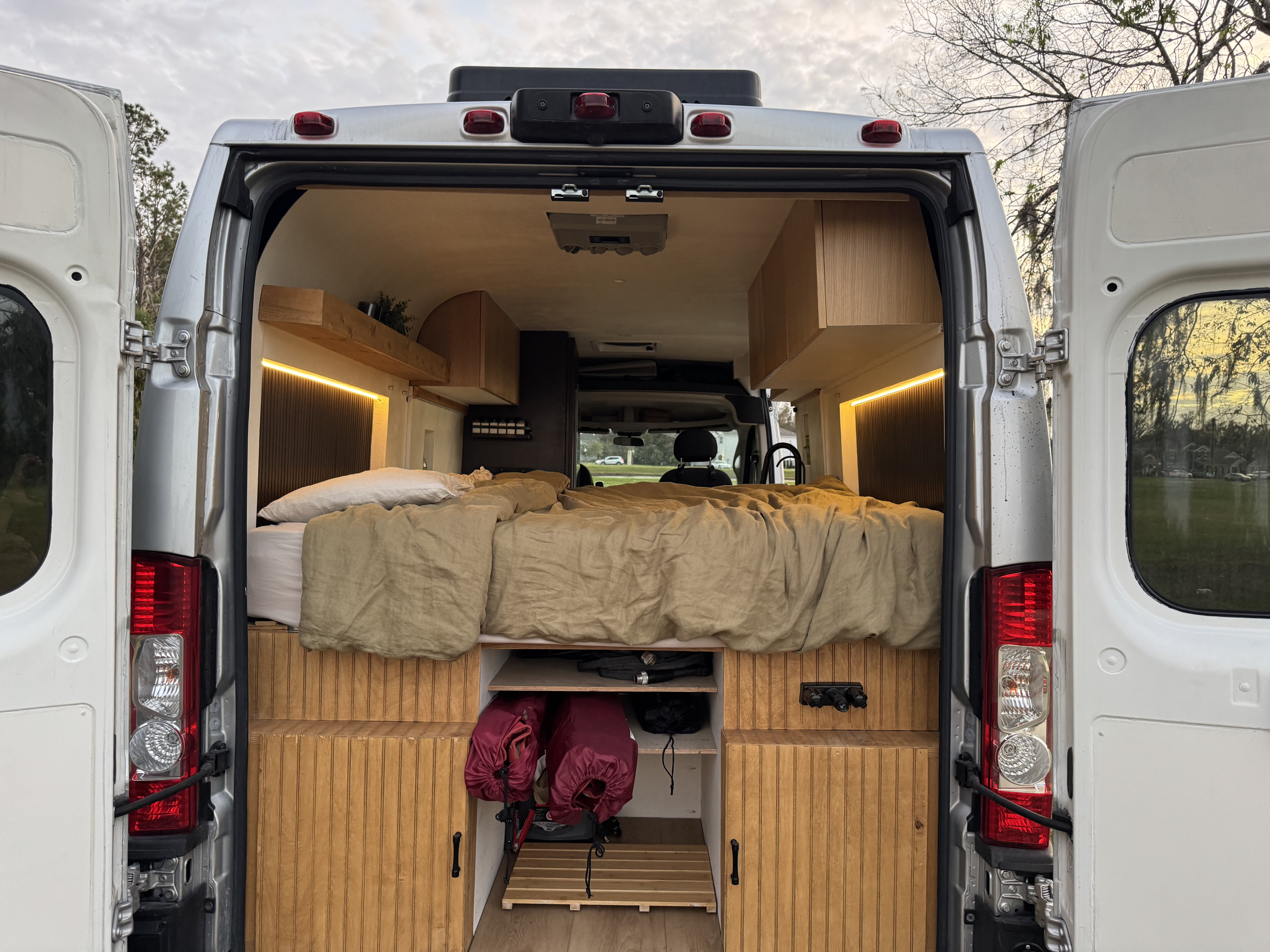 Rear view of an RV rental camper van, showing its cozy custom interior with a bed, storage, and wooden details.. Dodge Promaster 2500 2021