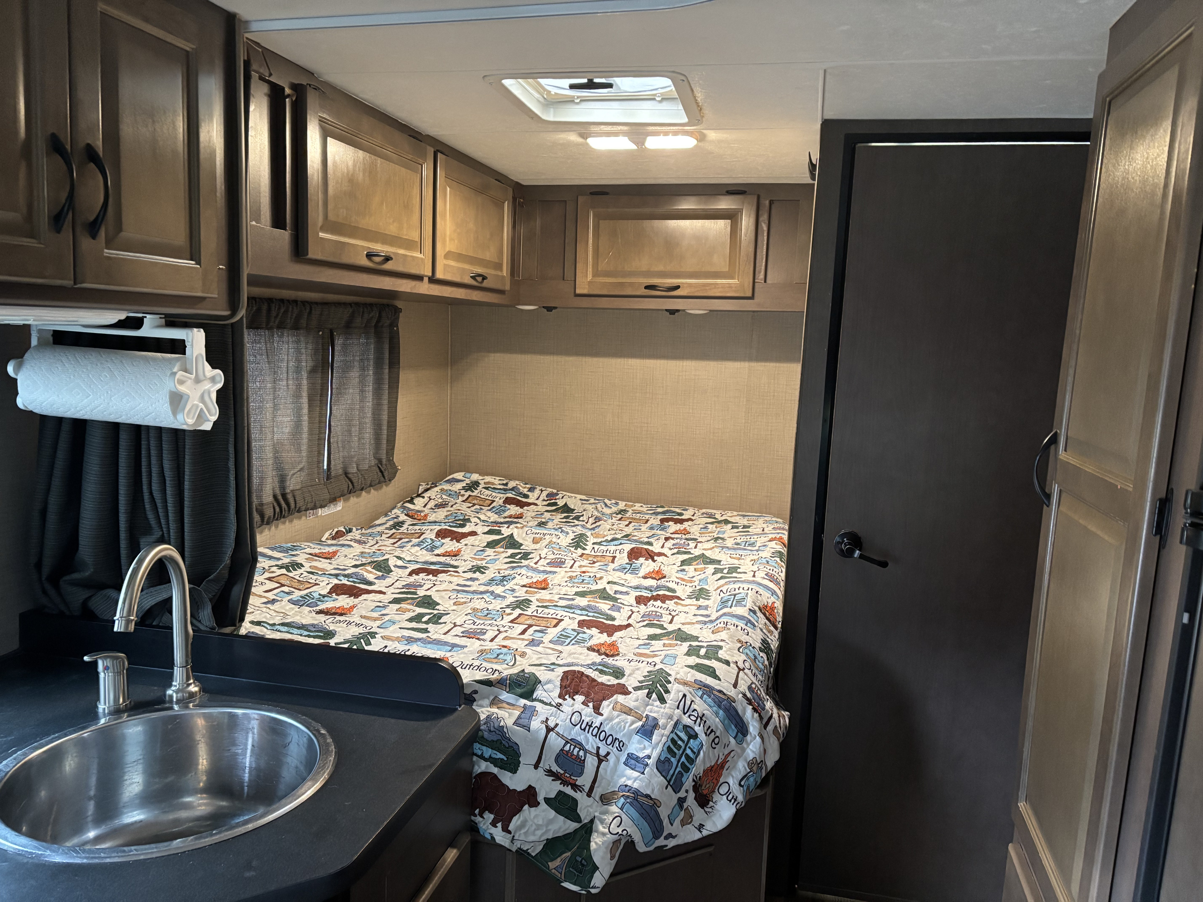 RV rental bedroom with nature-themed bed, small sink, and storage. Functional interior for camping trips.. Thor Majestic 2019