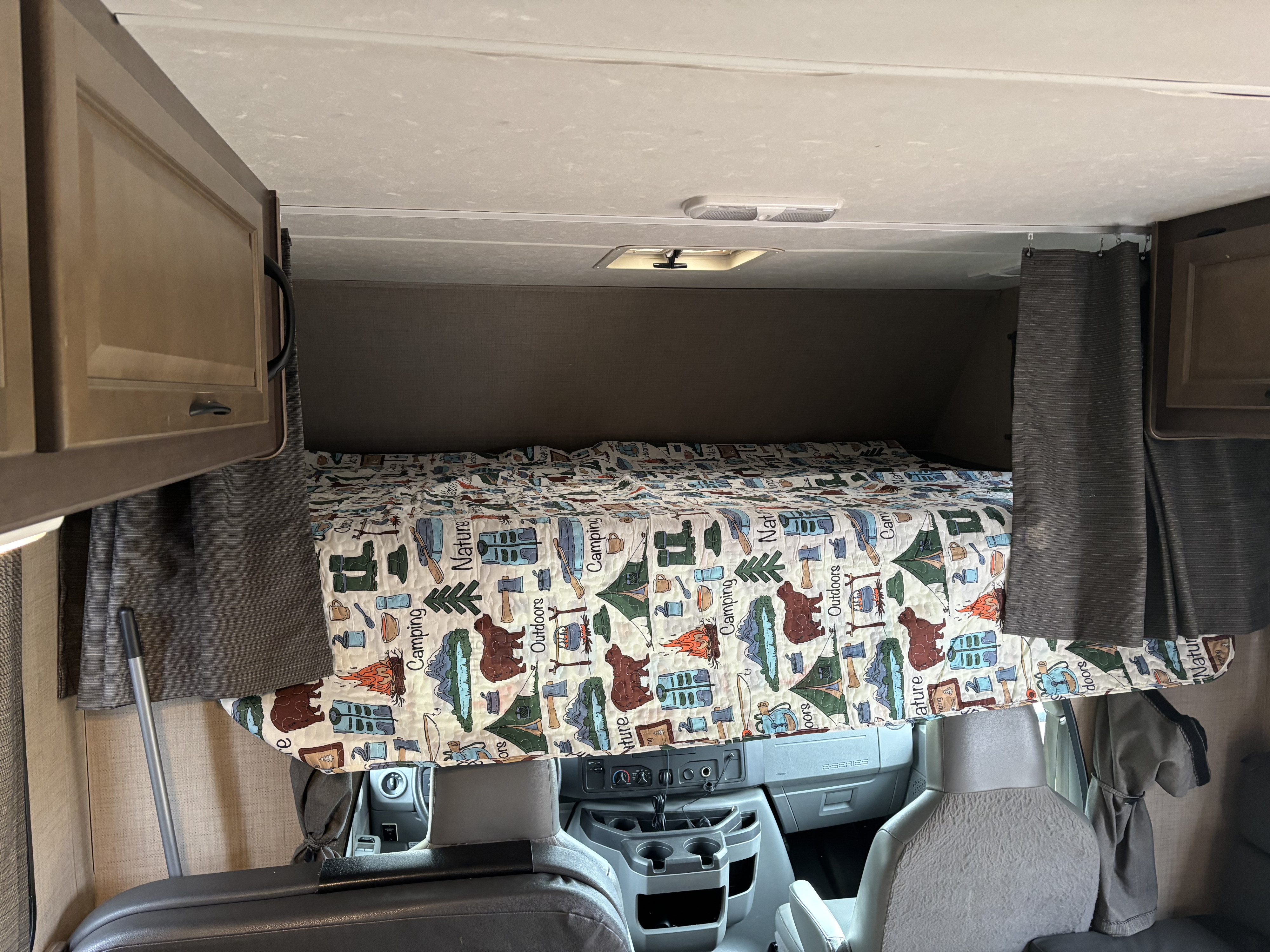 Cozy overhead bunk bed in an RV rental, featuring a fun camping-themed quilt above the driver's cabin area.. Thor Majestic 2019