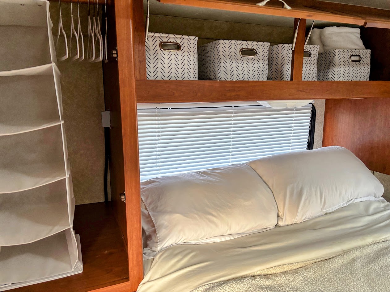 RV rental interior showing bedroom with hanging closet, storage bins, and bed with pillows. Organized travel space.. Four Winds 5000 2008