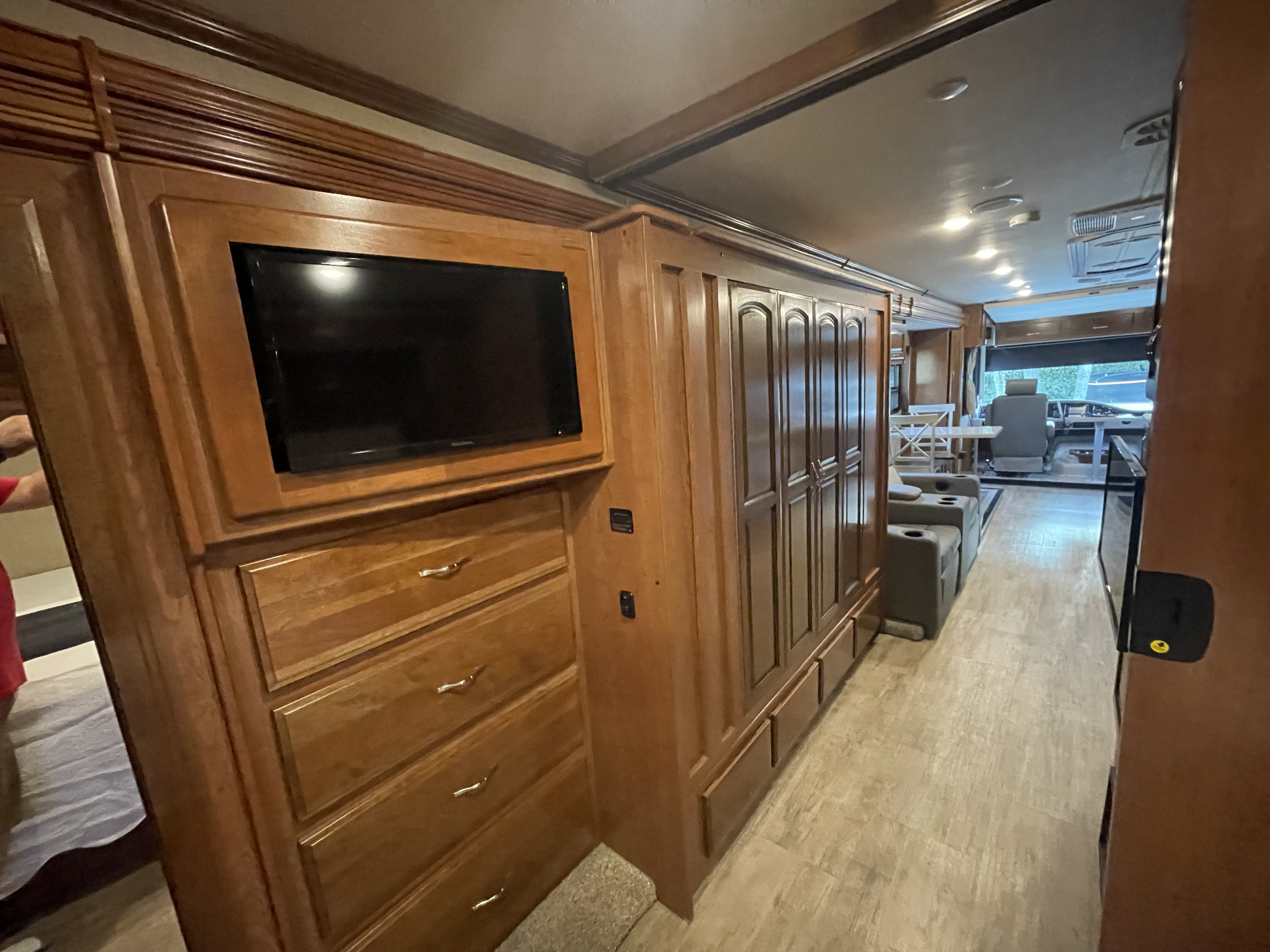 RV rental interior showing wood cabinetry, TV, bedroom dresser, and an open layout connecting to the living and cockpit areas.. Holiday Rambler Vacationer XE 2018
