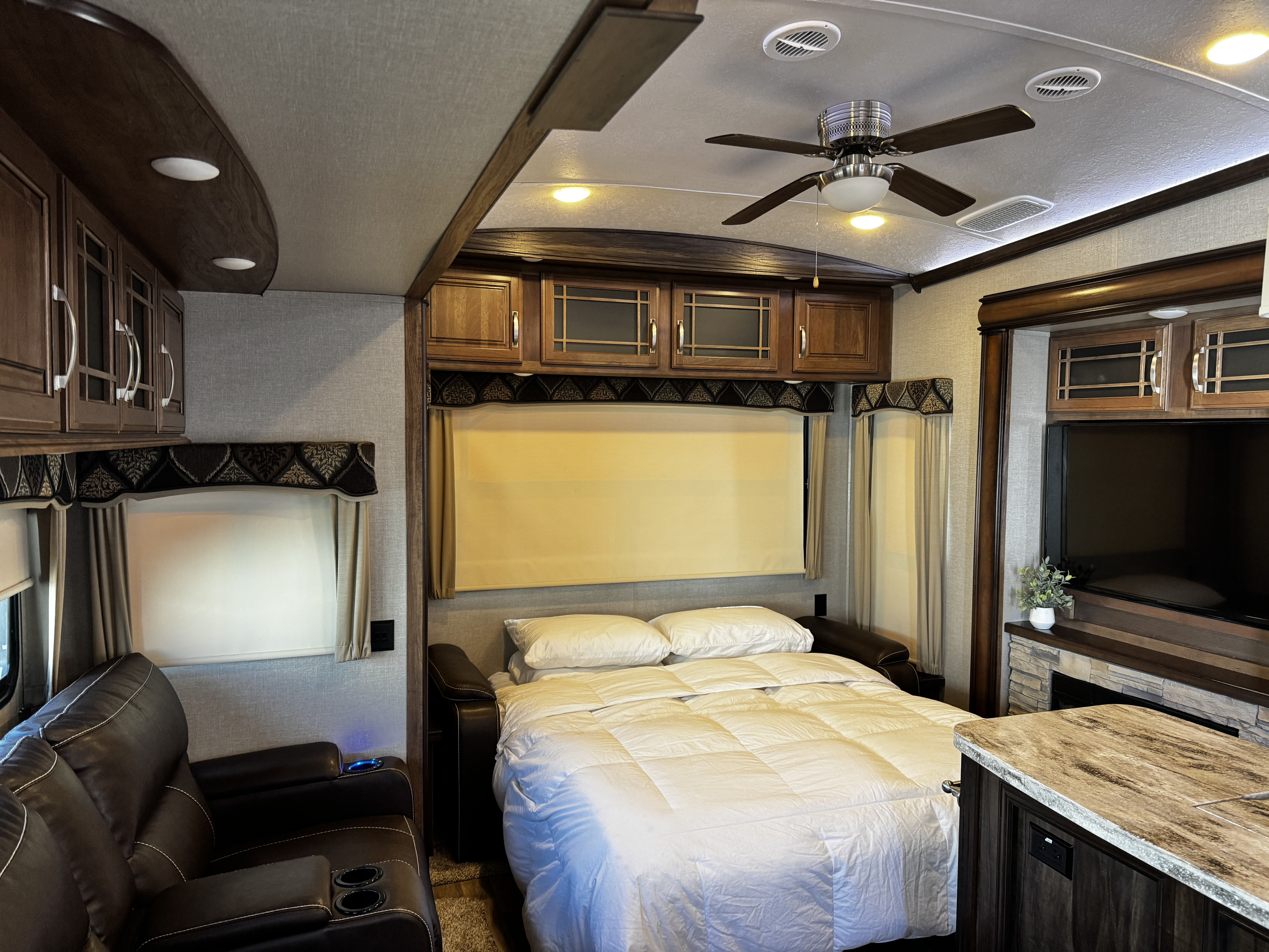 Cozy RV rental interior showcasing a comfortable bed, reclining sofa, ample cabinets, and a TV with fireplace.. Keystone RV Montana 2017