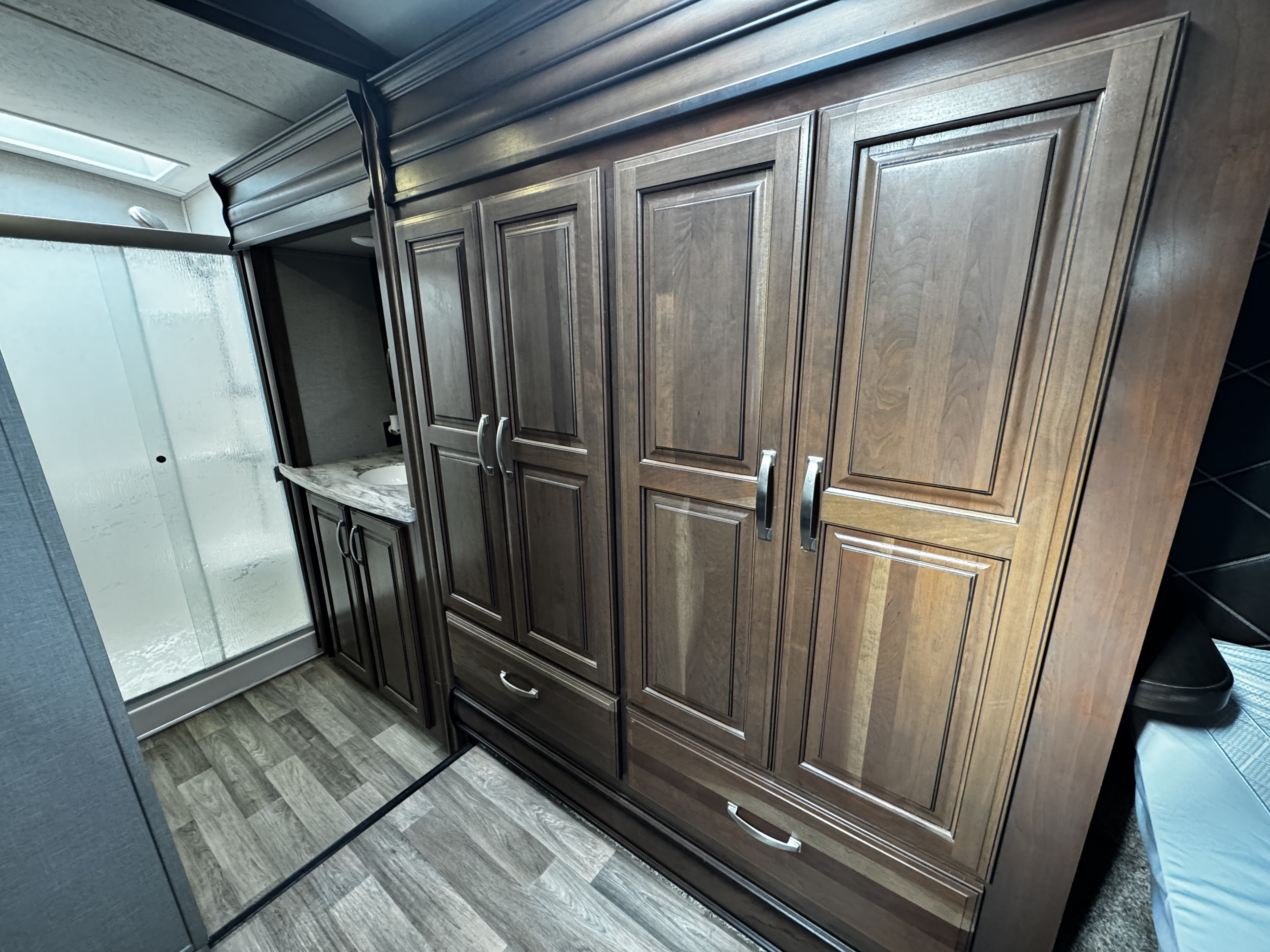 RV rental's bedroom & bath: Dark wood cabinets, shower, and sink are visible, creating a functional, compact interior.. Keystone RV Montana 2017