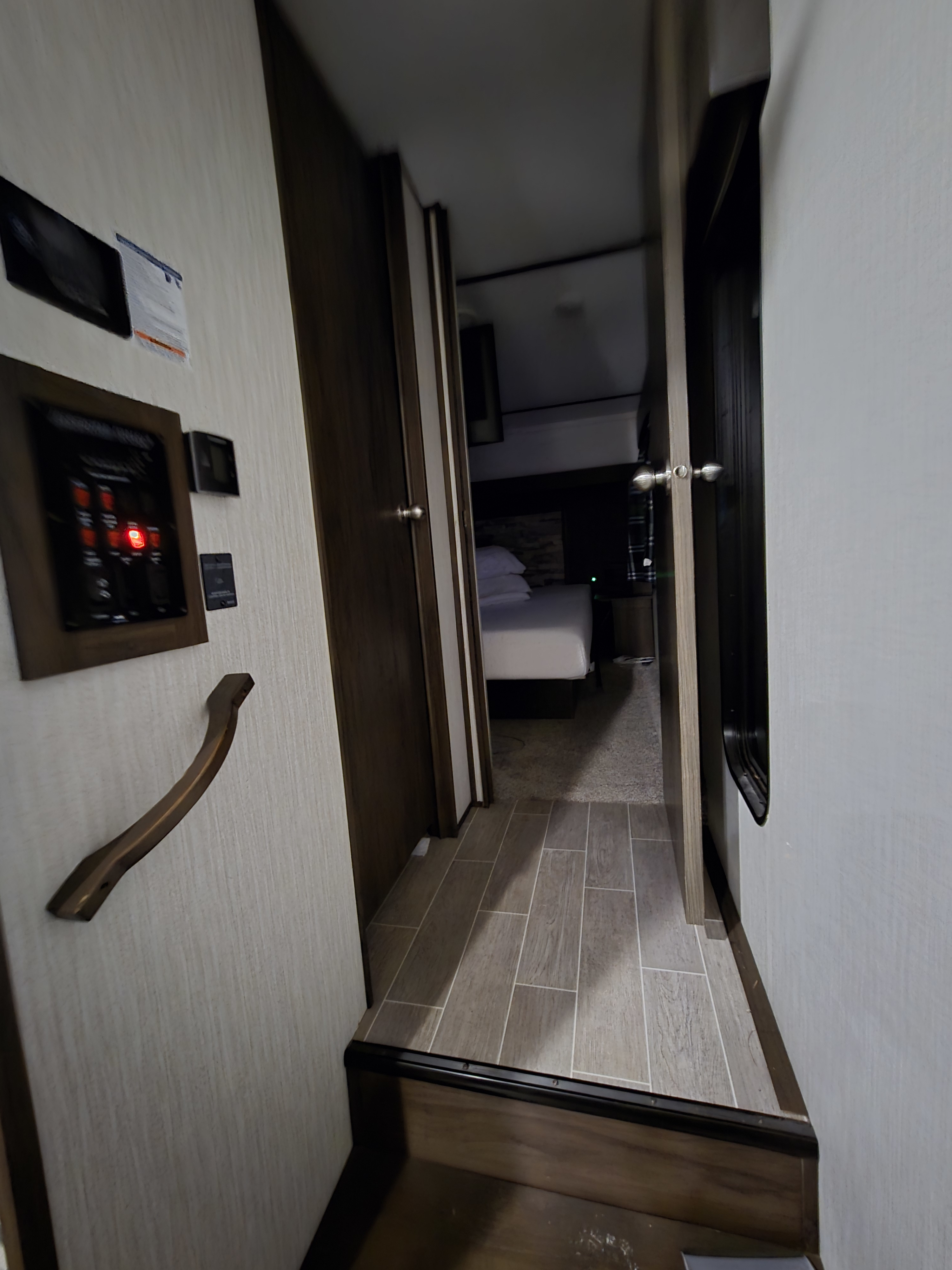 RV rental interior: narrow hallway leads to a bedroom with a white bed; a control panel is on the left wall.. Forest River Cherokee Arctic Wolf 2019