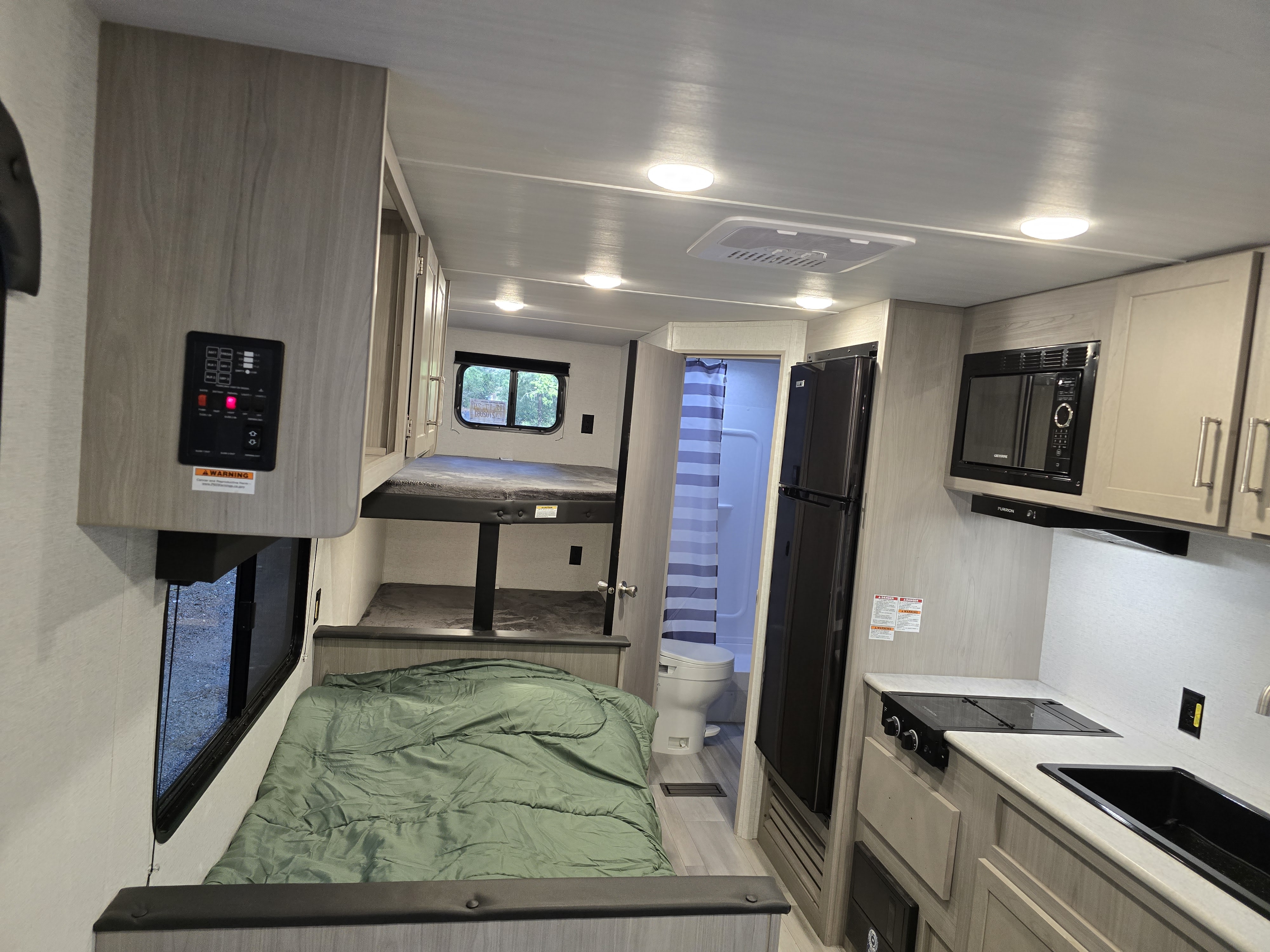 This RV rental interior features bunk beds, a main bed, kitchen with sink, stove, microwave, fridge, and bathroom.. Keystone RV Springdale 2024