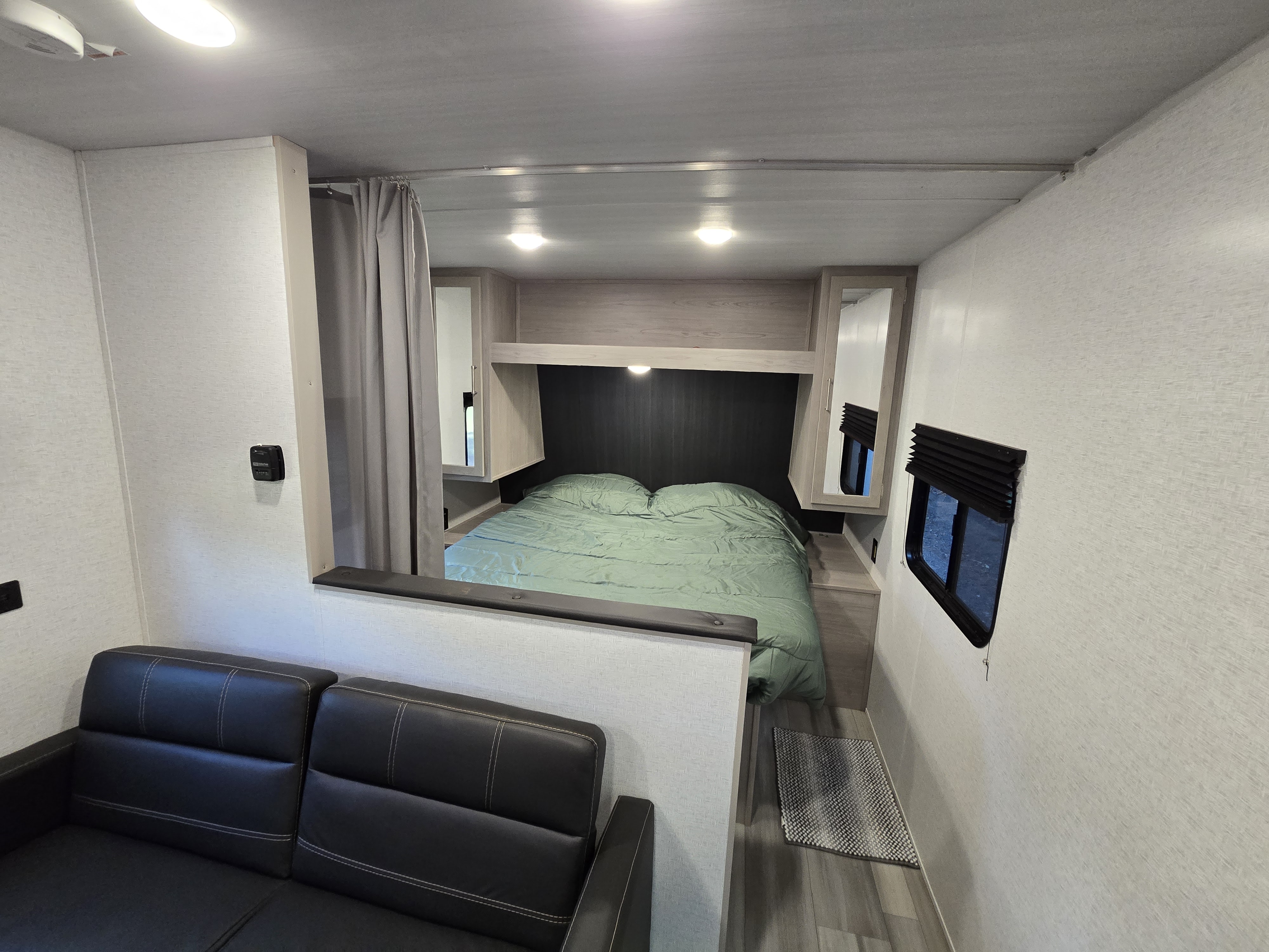 Experience our RV rental: features a cozy bedroom with green bedding, practical storage, and a comfy sofa living area.. Keystone RV Springdale 2024