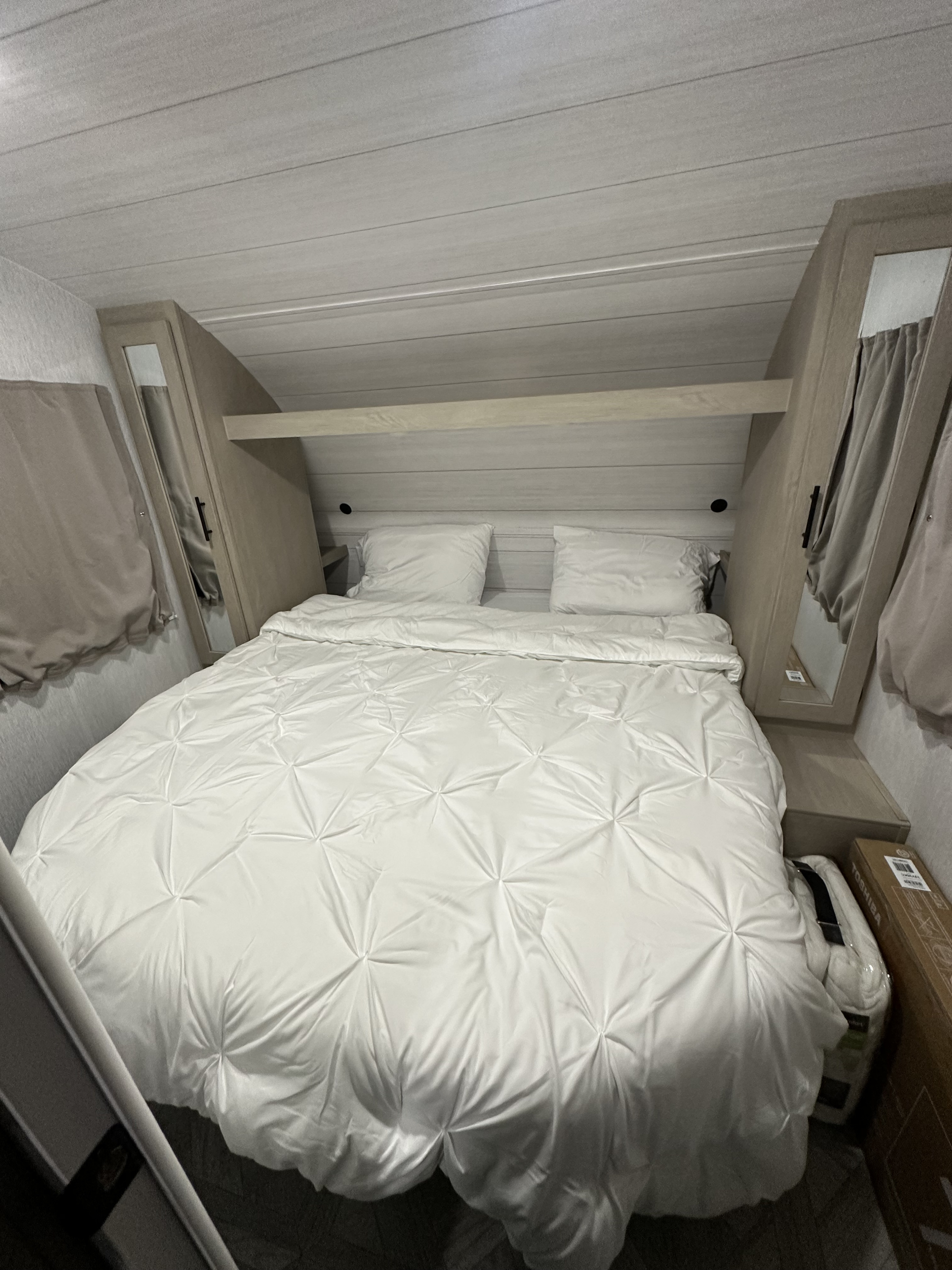 Cozy, well-appointed RV rental bedroom with a large white bed, built-in storage, and light wood-paneled walls. Perfect for travel.. Forest River Salem Cruise Lite 2024