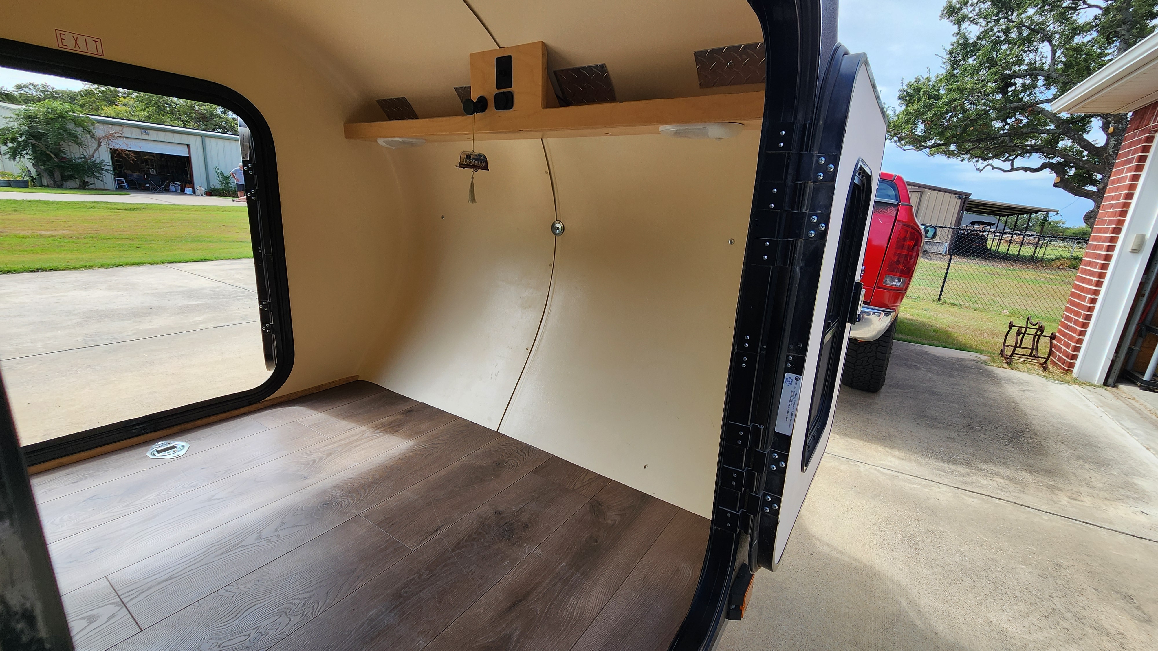 Interior of an rv rental, featuring wood-look flooring, a shelf, and open door view. Outside, a red truck and building are visible.. High Altitude XT50 Treardrop Camper 2022