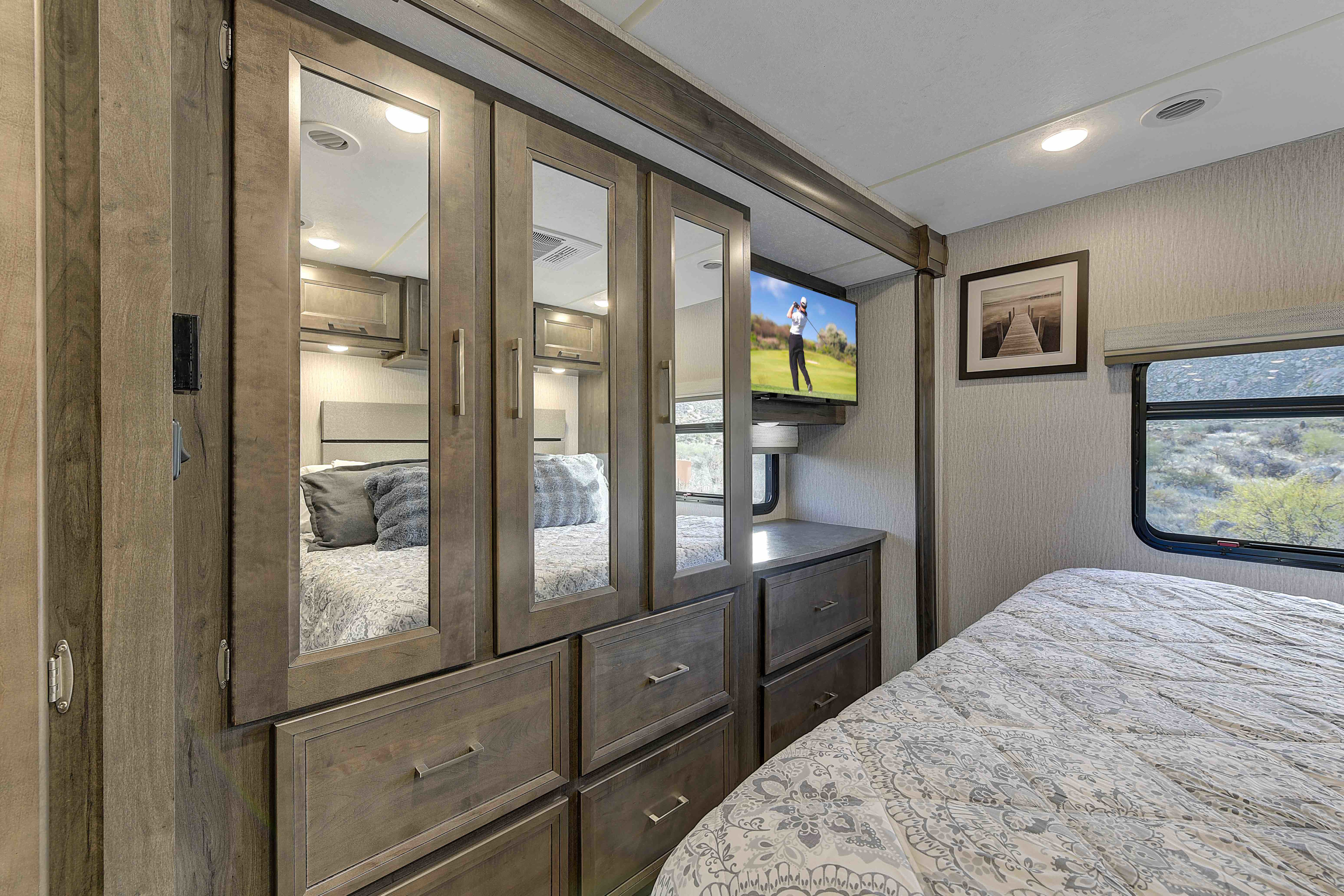 Spacious RV rental bedroom featuring a mirrored wardrobe, dresser, mounted TV, and comfortable bed with a window view.. Coachmen Mirada 35OS 2023