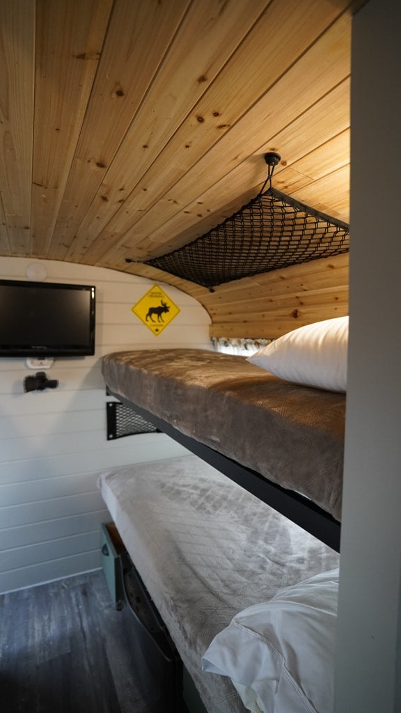 Inside an RV rental: Compact space with two bunk beds, wall-mounted TV, wooden ceiling, and an overhead storage net.. Bluebird TC3000 2008