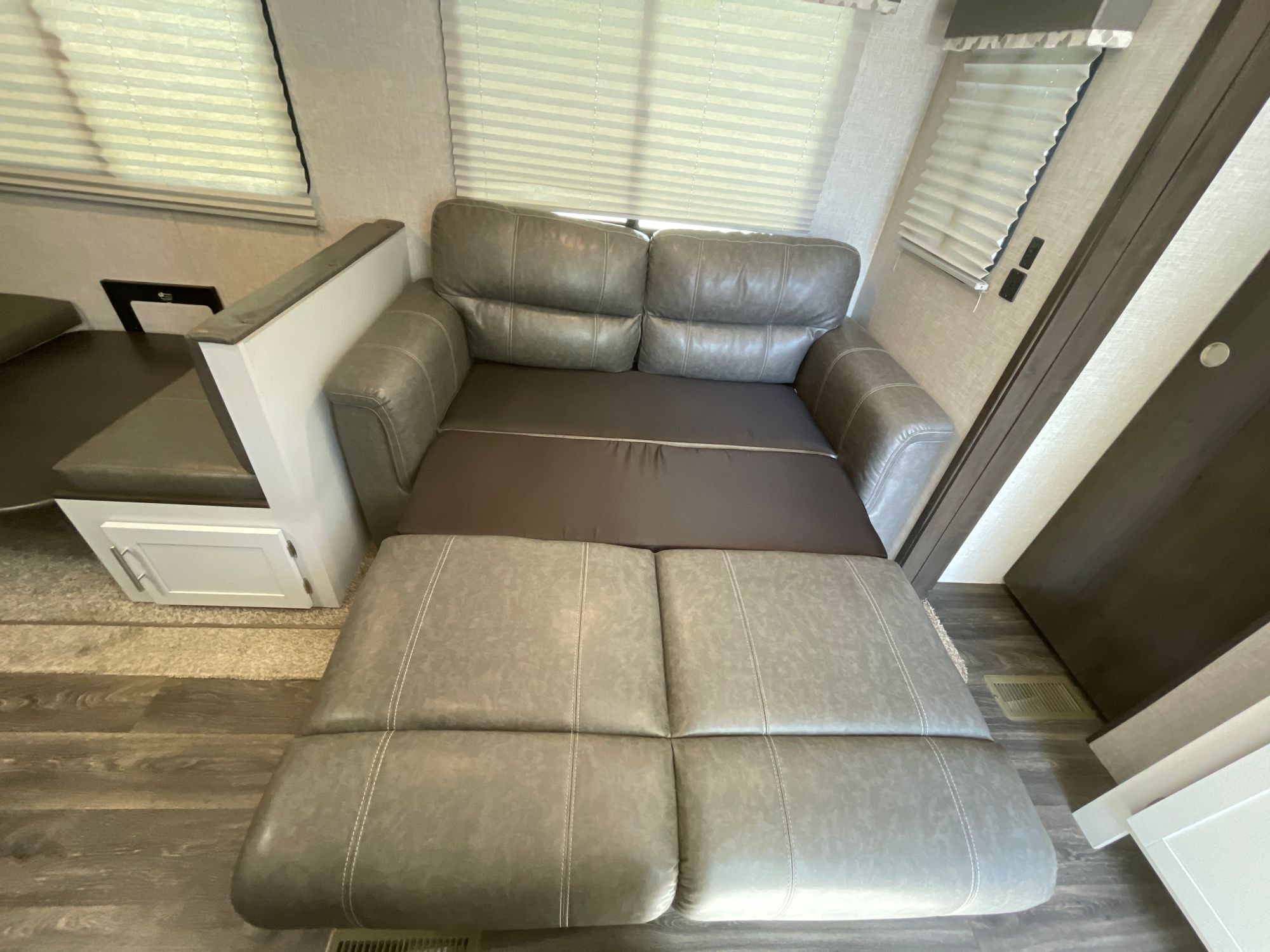 Versatile RV rental interior featuring a gray pull-out sofa bed extended, beside a dinette area with blinds. Ideal for trips.. Keystone RV Bullet Ultra Lite 2021
