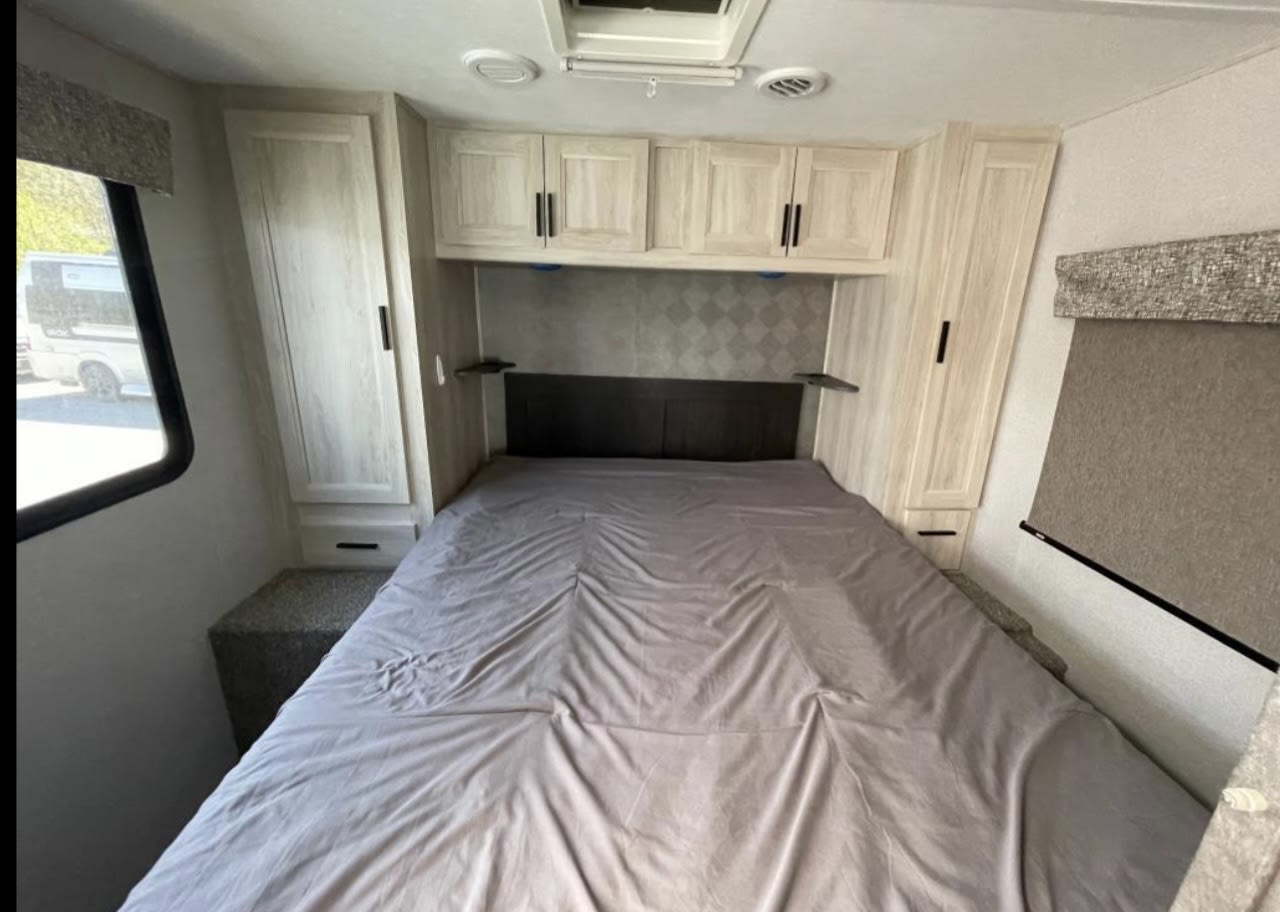 Inside an RV rental: a cozy bedroom with a bed, ample storage in overhead and side cabinets, plus window and shade.. Forest River Forester 2020
