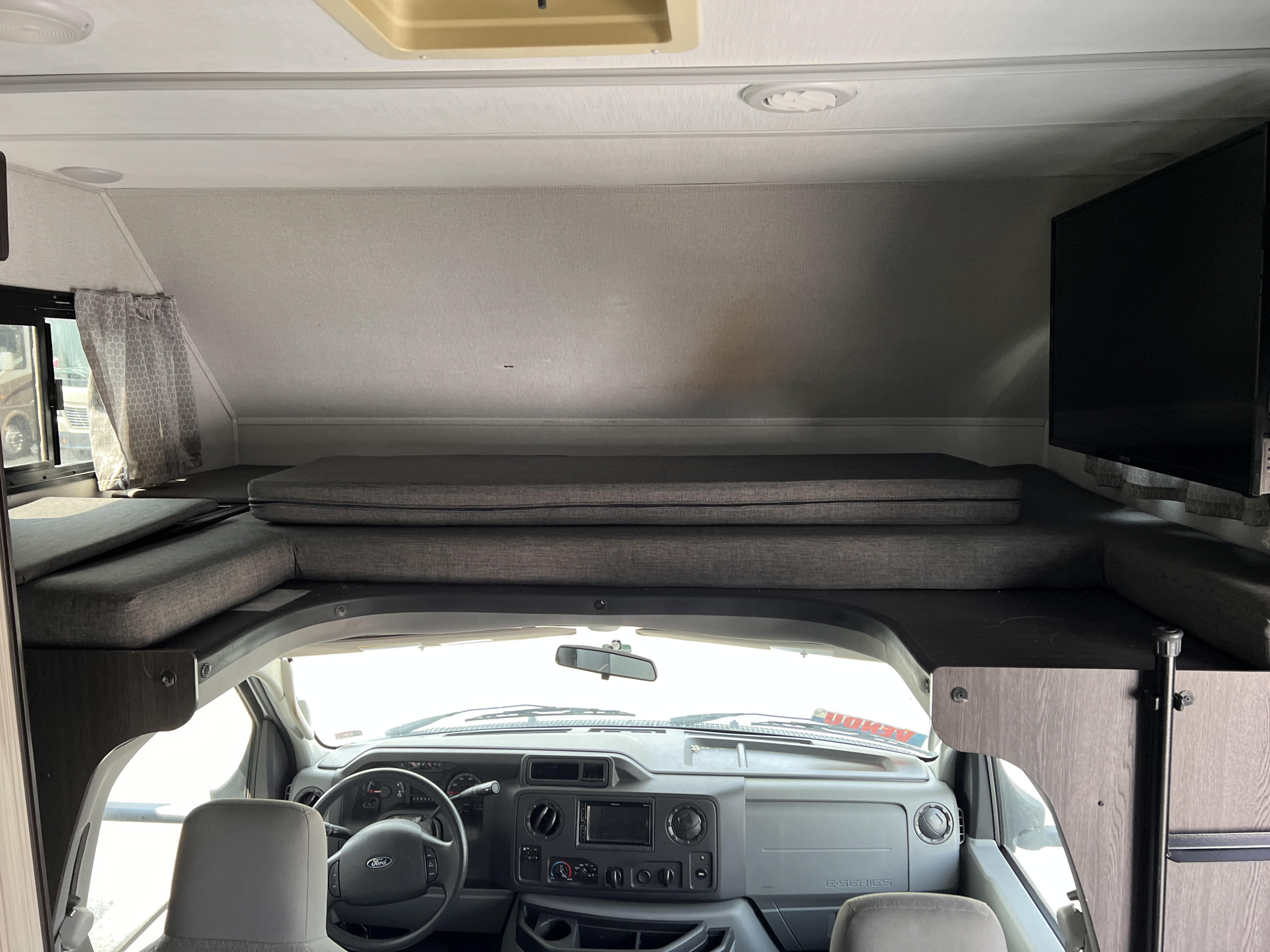 RV rental interior: View of the over-cab bunk with gray cushions, driver's dashboard, and front seats, offering comfortable travel.. Forest River Forester 2020