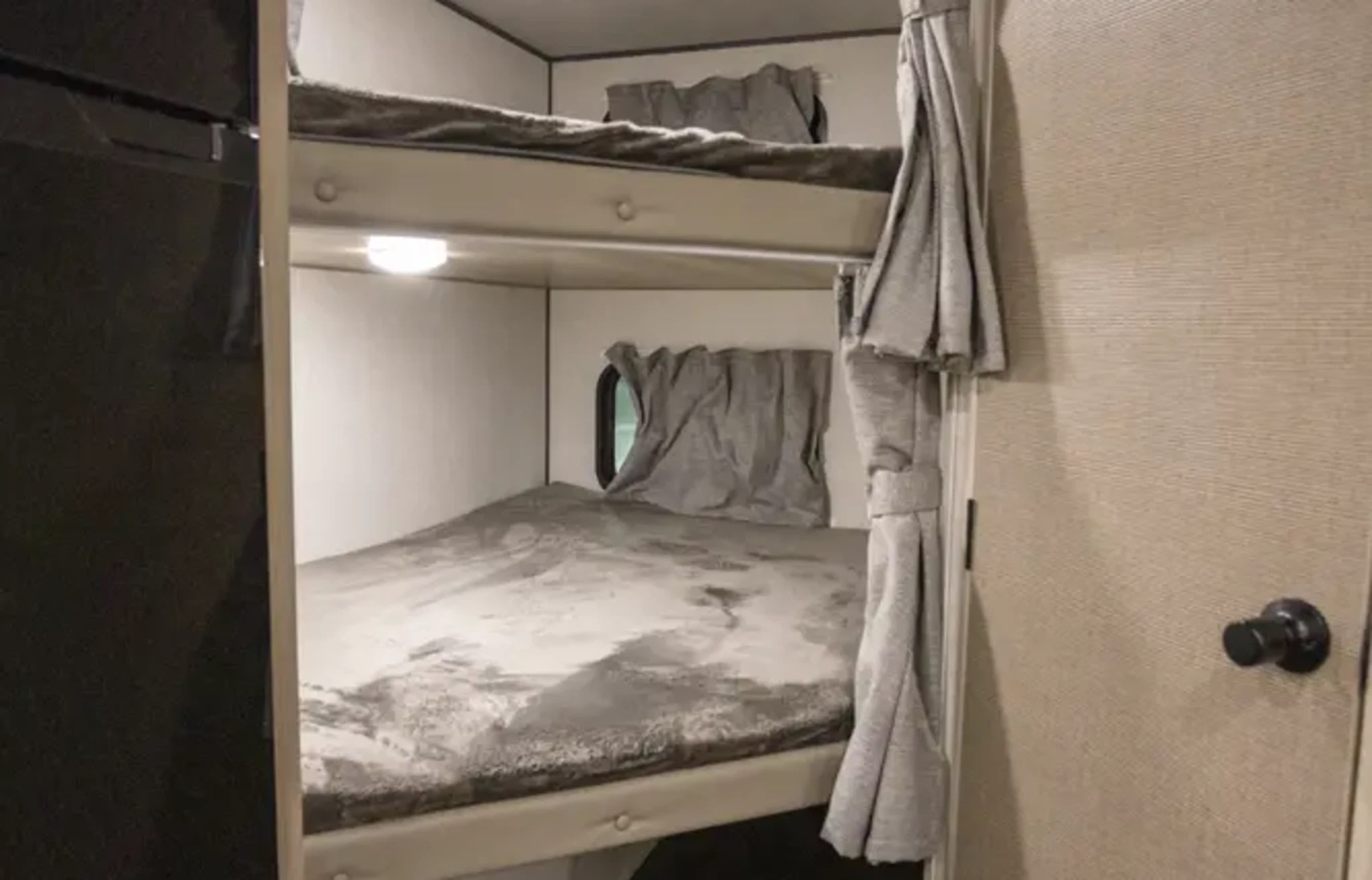 RV rental shows stacked bunk beds with gray bedding and curtains. A window and task light are visible for comfortable stays.. Wildwood FSX Forest River RV 2025