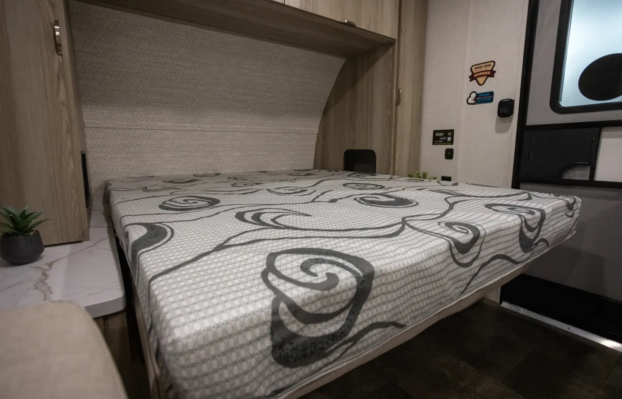 This RV rental's bedroom offers a cozy bed with a modern grey patterned mattress, wood cabinetry, and smart storage solutions.. Wildwood FSX Forest River RV 2025