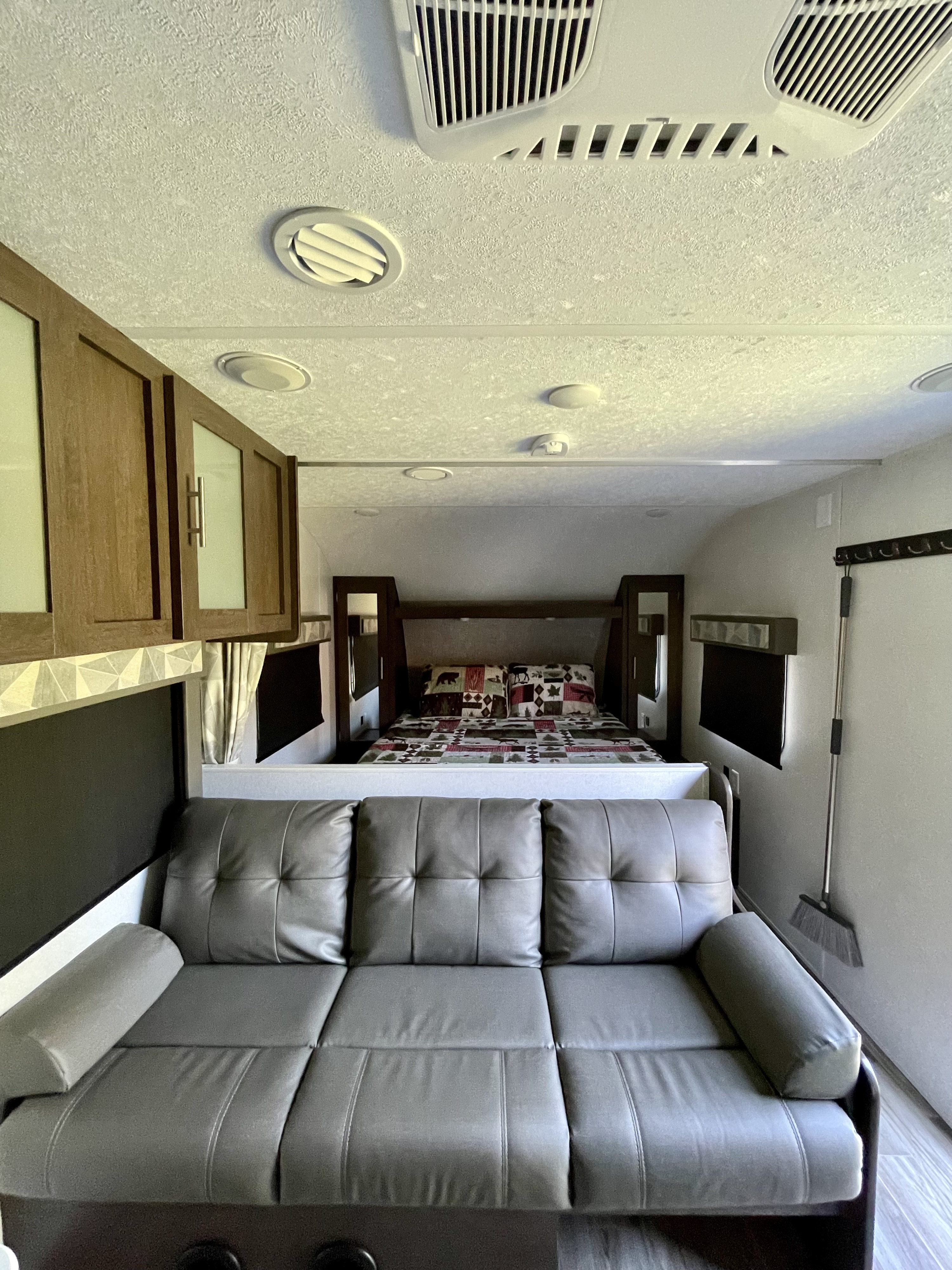 Inside this RV rental, a gray sofa faces a cozy bed with patterned bedding. Overhead cabinets and ceiling vents complete this compact living space.. Forest River Salem Cruise Lite 2019