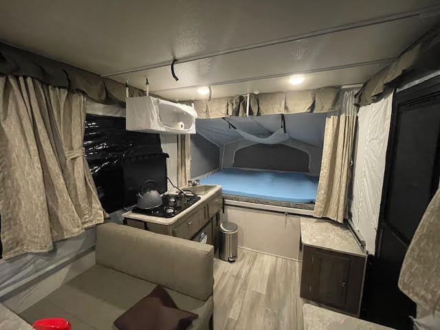 Inside an RV rental pop-up camper, featuring a compact kitchen, comfortable bed, and living area with sofa.. Forest River Rockwood ESP 2022