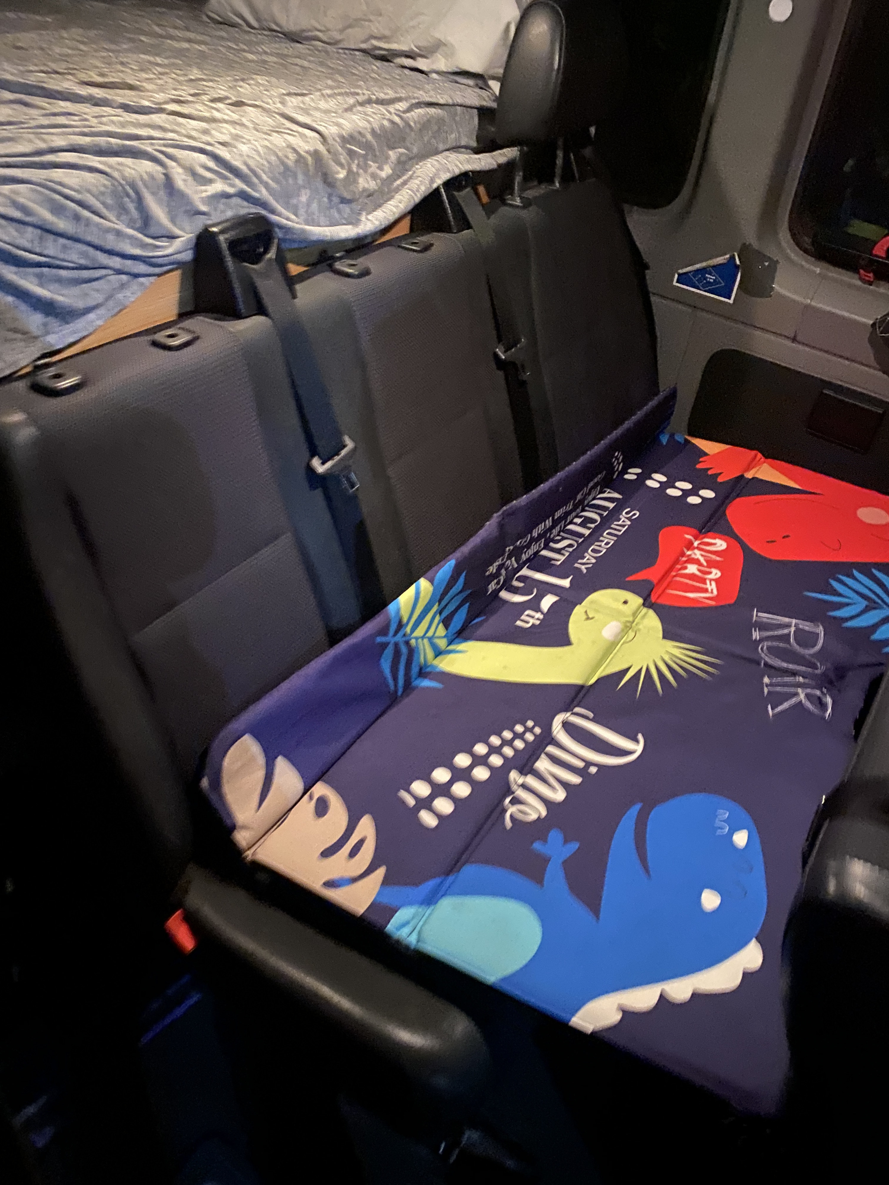 RV rental camper van interior featuring a cozy bed, passenger seats, and a fun dinosaur mat for kids.. Mercedes Sprinter 2011