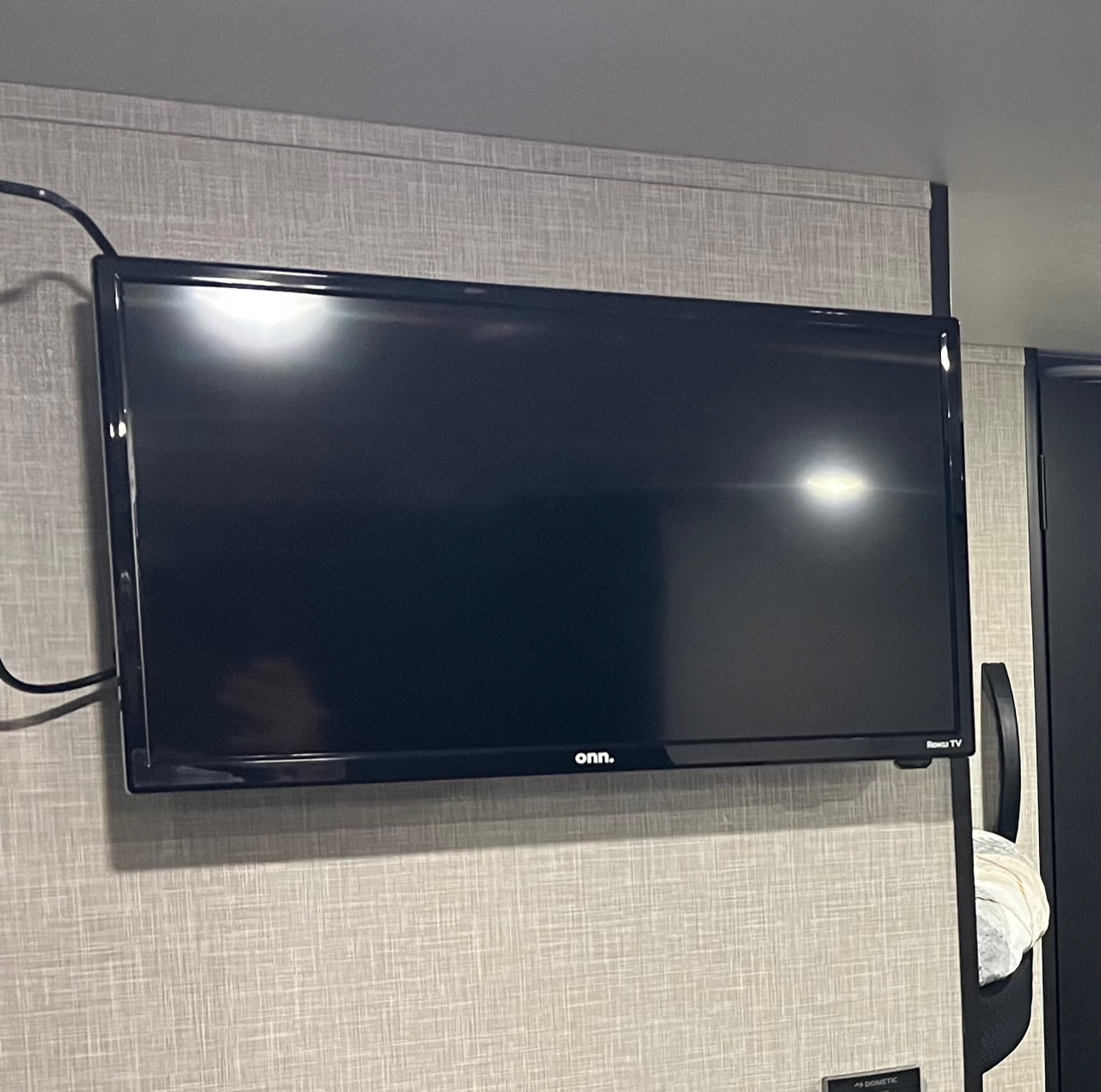 An Onn. Roku TV mounted on a textured wall inside an RV rental, with visible cables and screen reflections.. Jayco Jay Flight SLX 260BH 2025