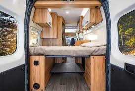 Peek inside this RV rental! A cozy bed, wooden cabinets, and clever under-bed storage in a modern camper van setup.. FONT VENDOME Terravan 2025