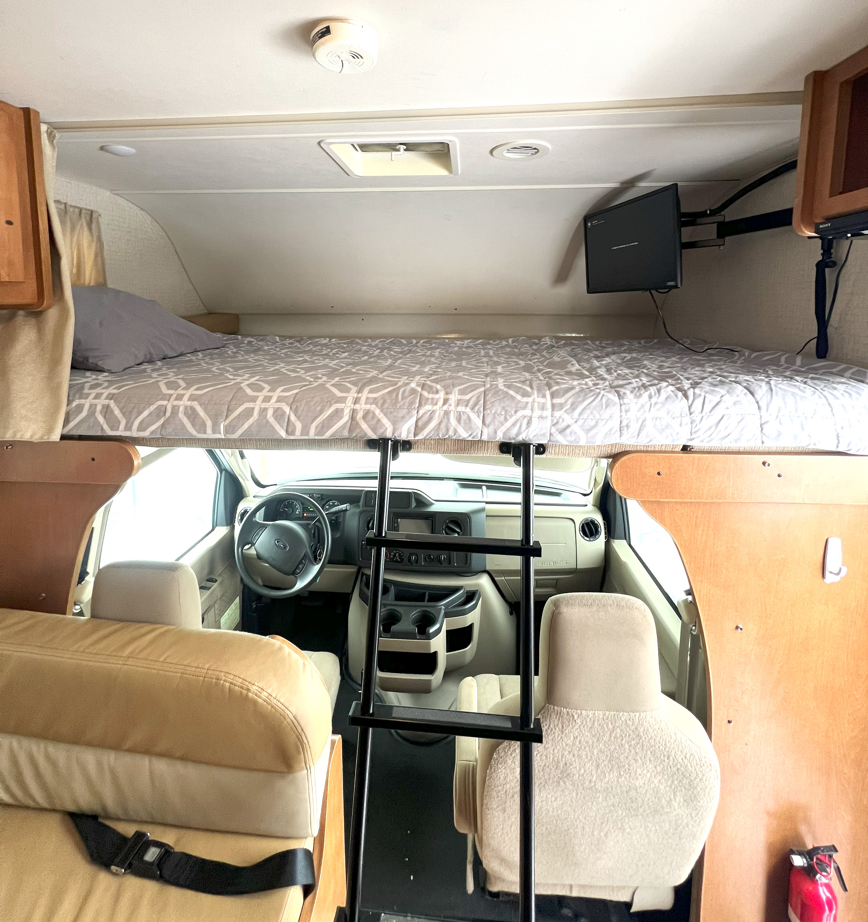 Inside an RV rental: a comfortable cab-over bed with a ladder leading down to the front driver's cockpit.. Winnebago Spirit 22R 2016