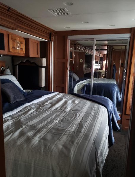 Comfortable RV rental bedroom featuring a large bed, wood cabinetry, and mirrored closets, perfect for your travels.. Fleetwood Discovery 2013